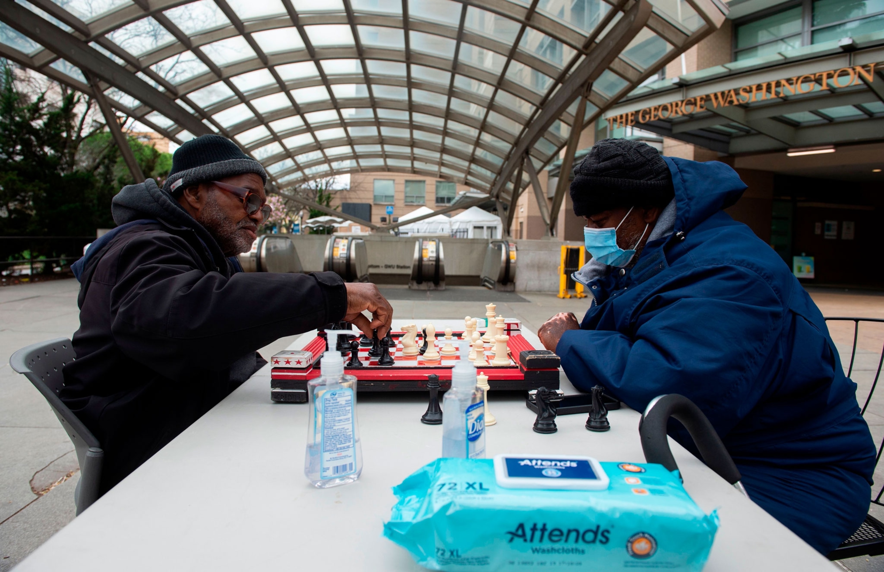 two people playing chess outside with bottles of hand sanitizer and wipes