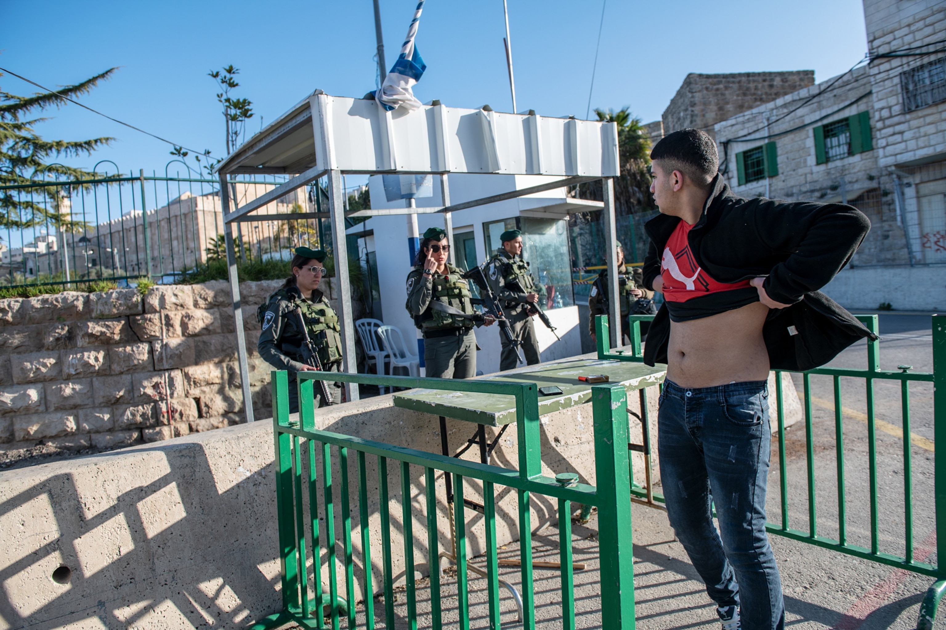 a man lifting his shirt to show soldiers he isn't hiding weapons