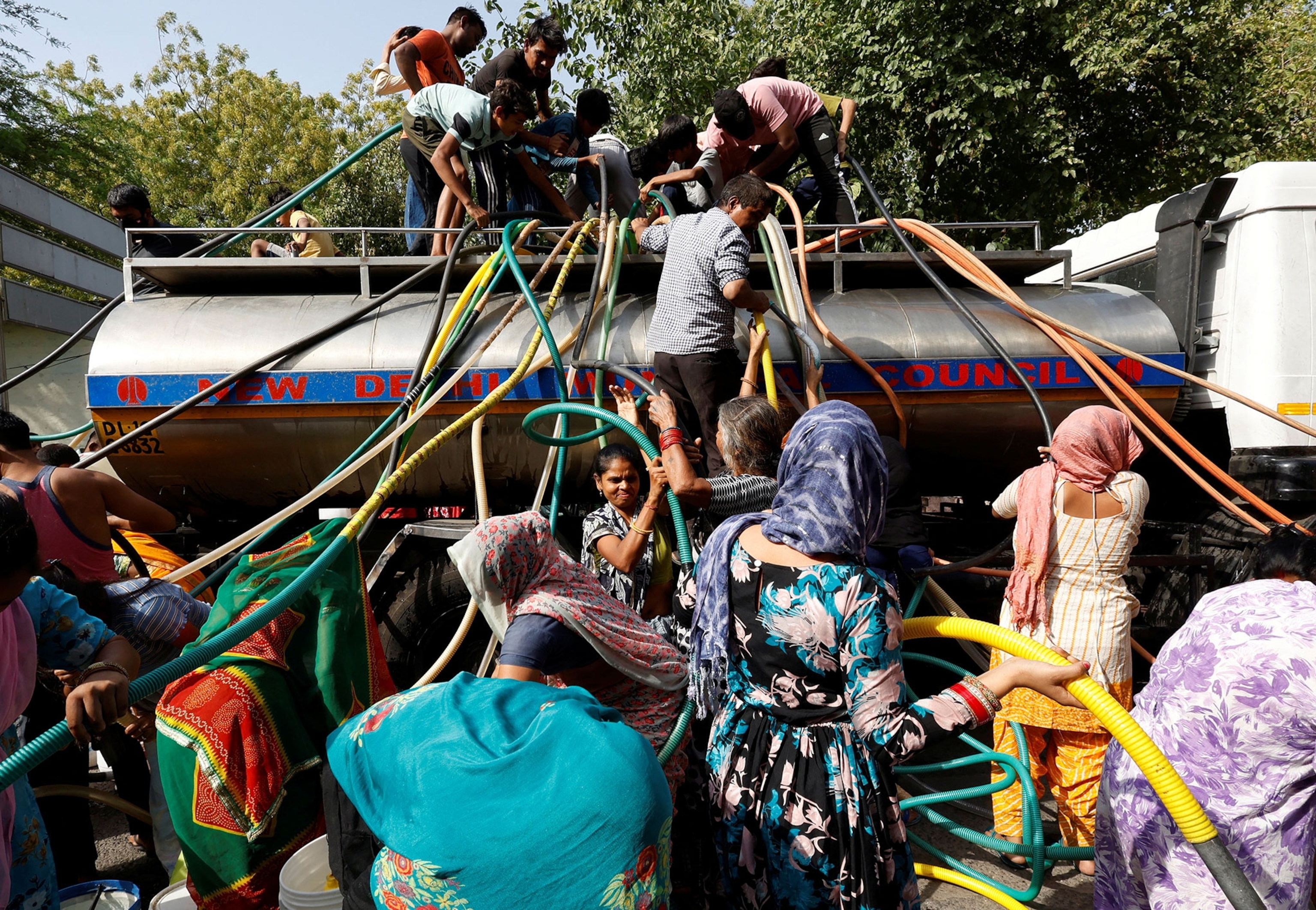 Residents use pipes to fill their containers with drinking water from a water tanker during a hot day in New Delhi, India. Some residents stand atop the truck, while others receive water below.