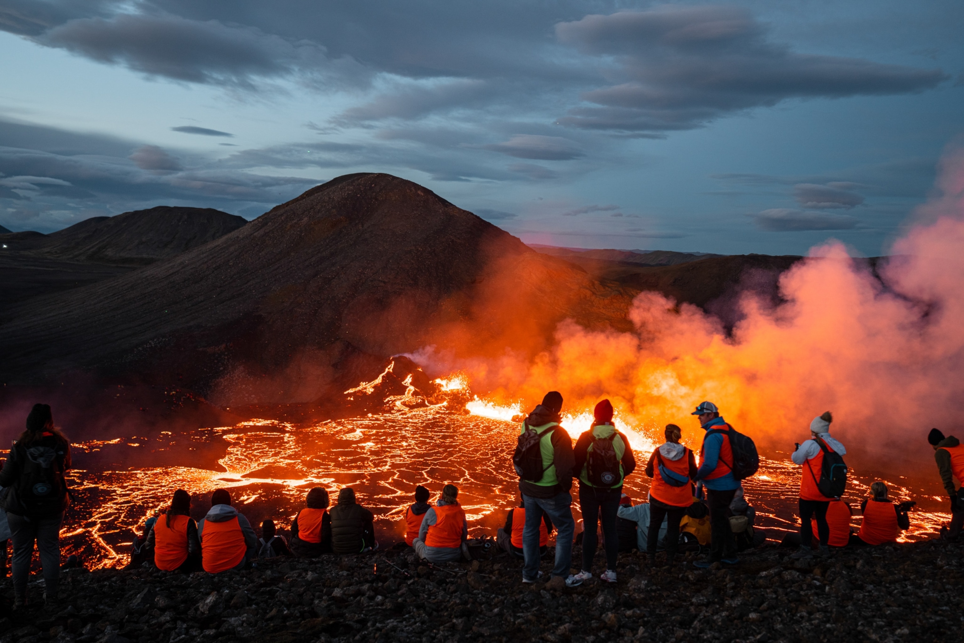 A group of people stand at the foot of an active volcano