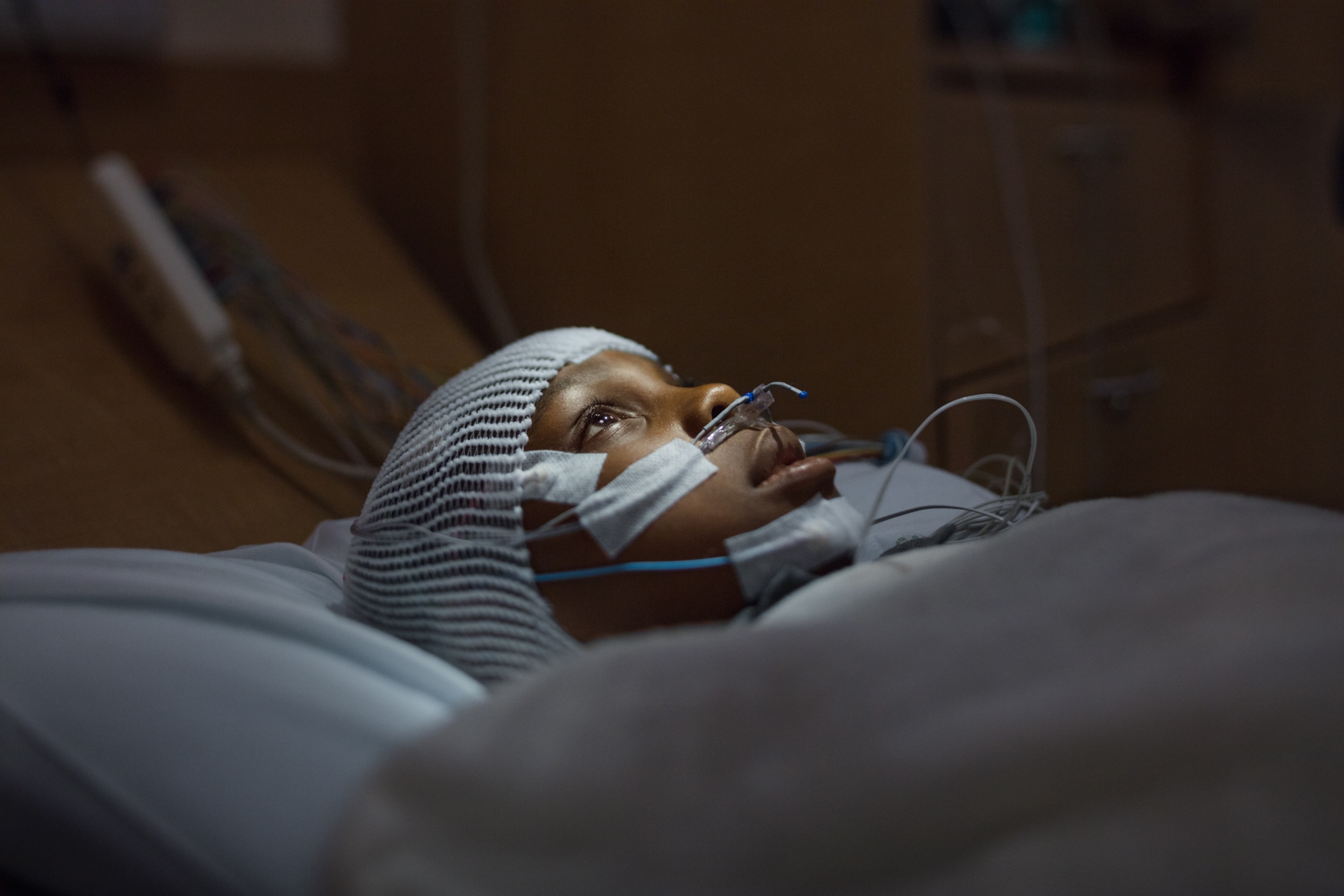a young boy wearing a cap with wires laying in bed as he looks up