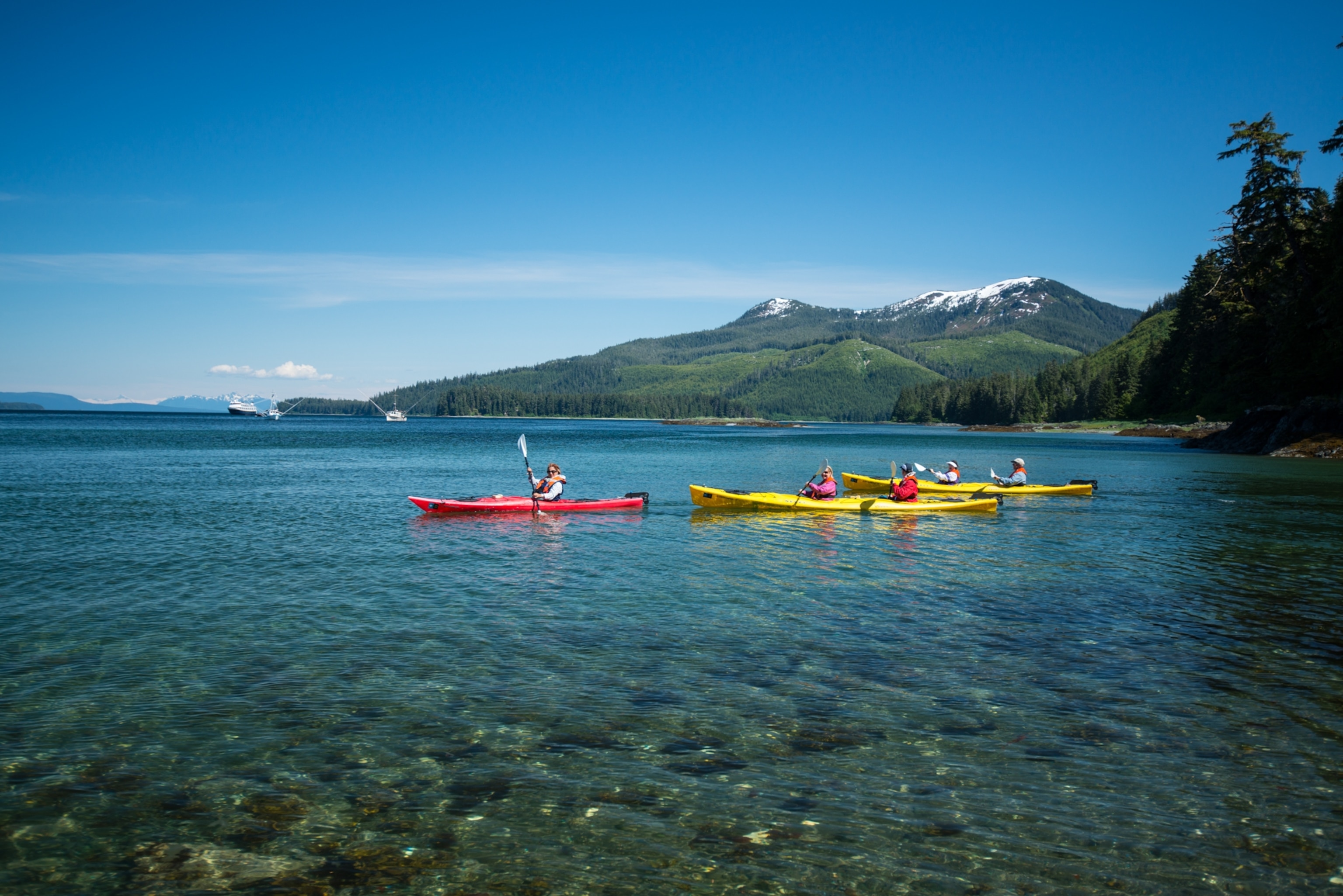 A group kayaking on crystal clear water with mountains in the background.