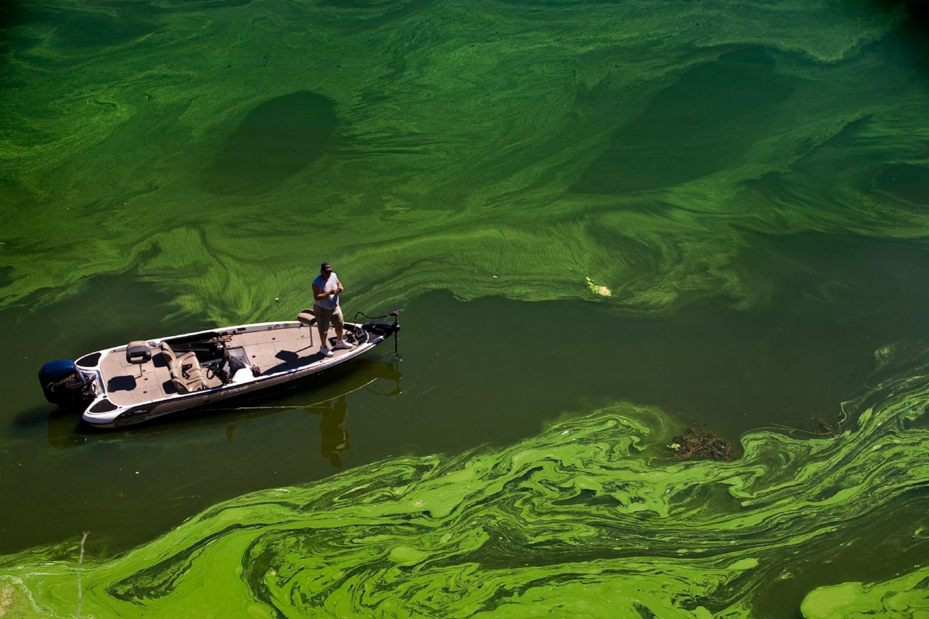 A man standing on a boat surrounded by green water.