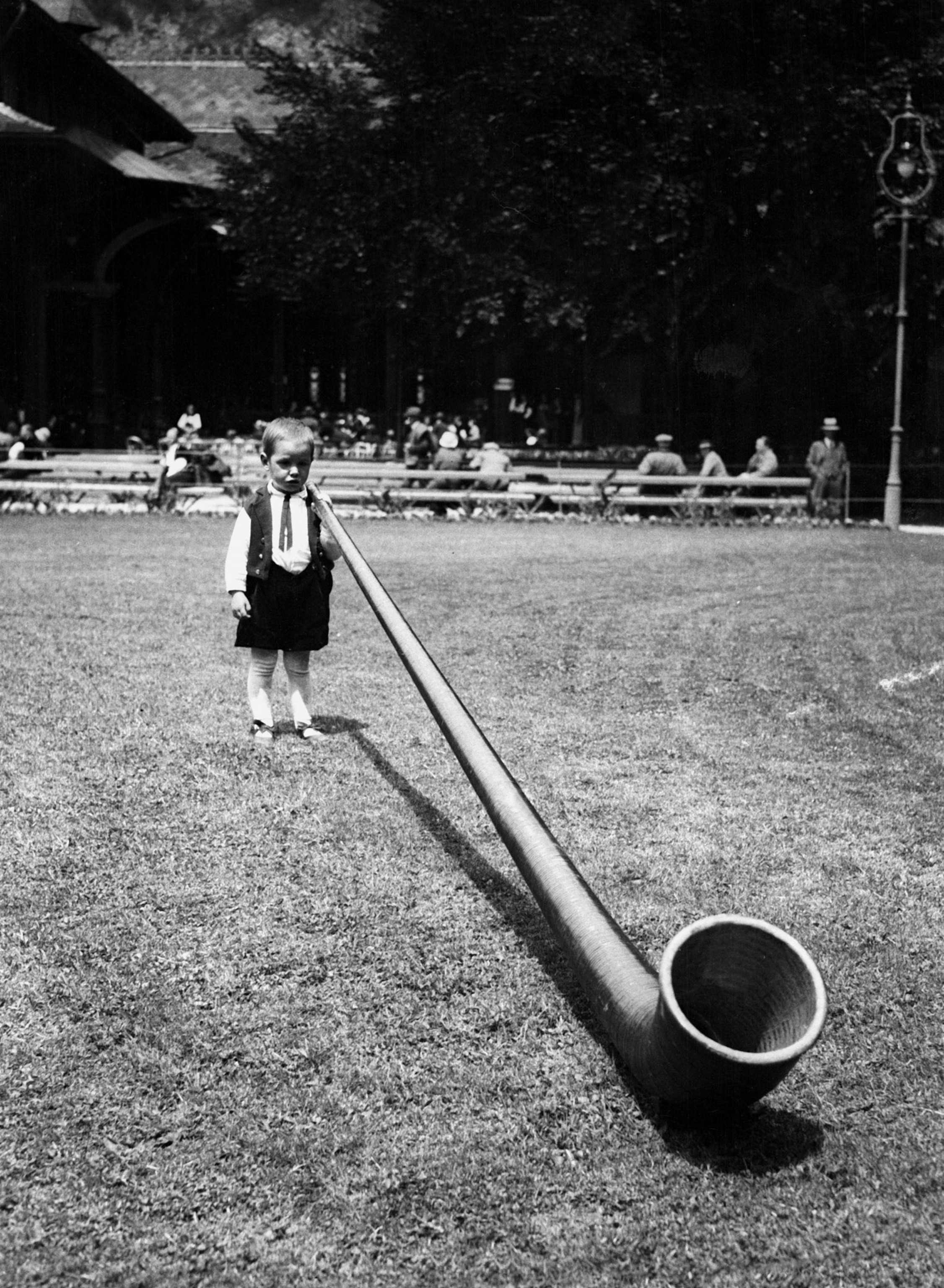 a black and white photograph of a young boy with an alphorn more than double his size