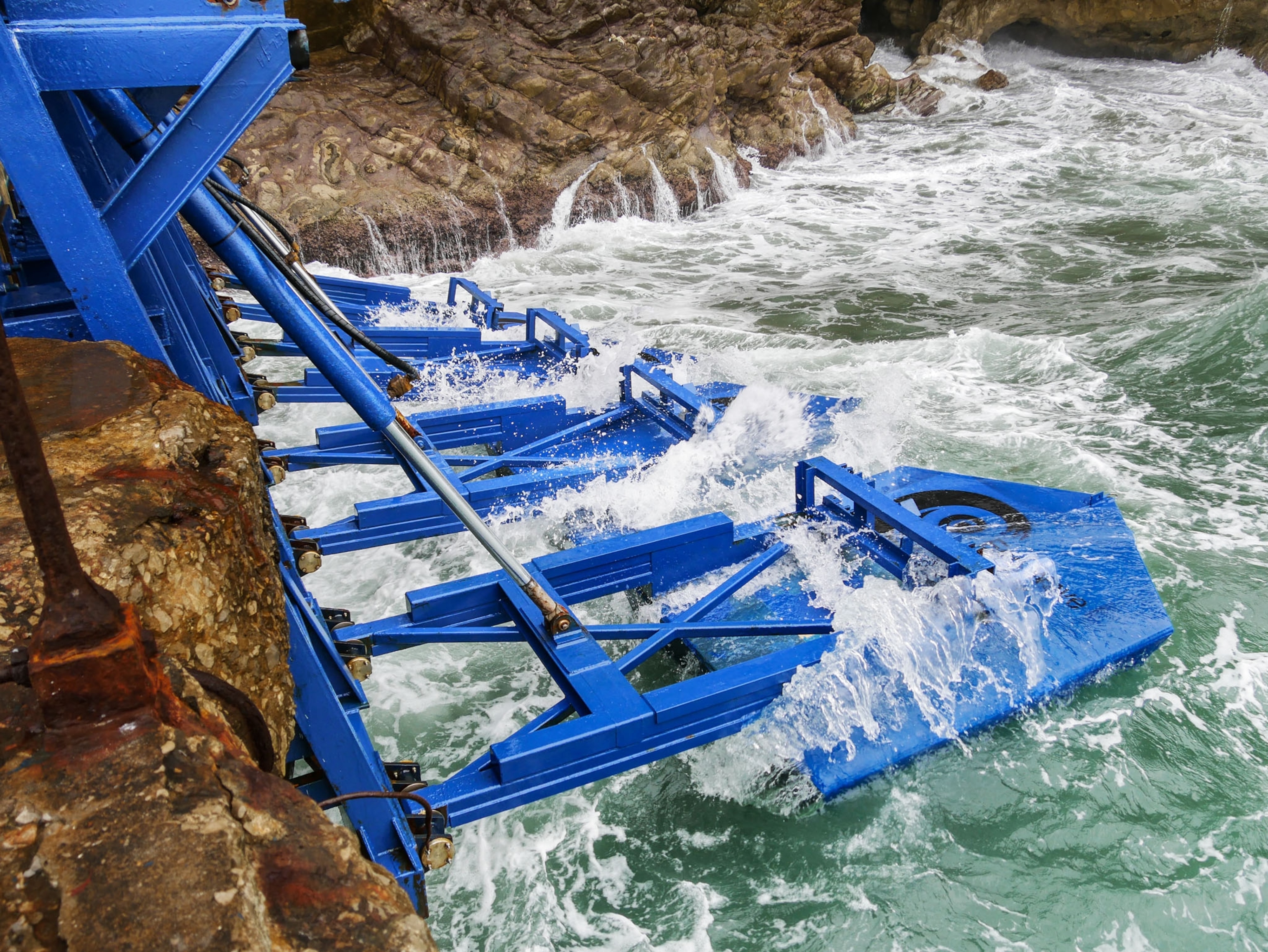 blue structure suspended from cliff into ocean.