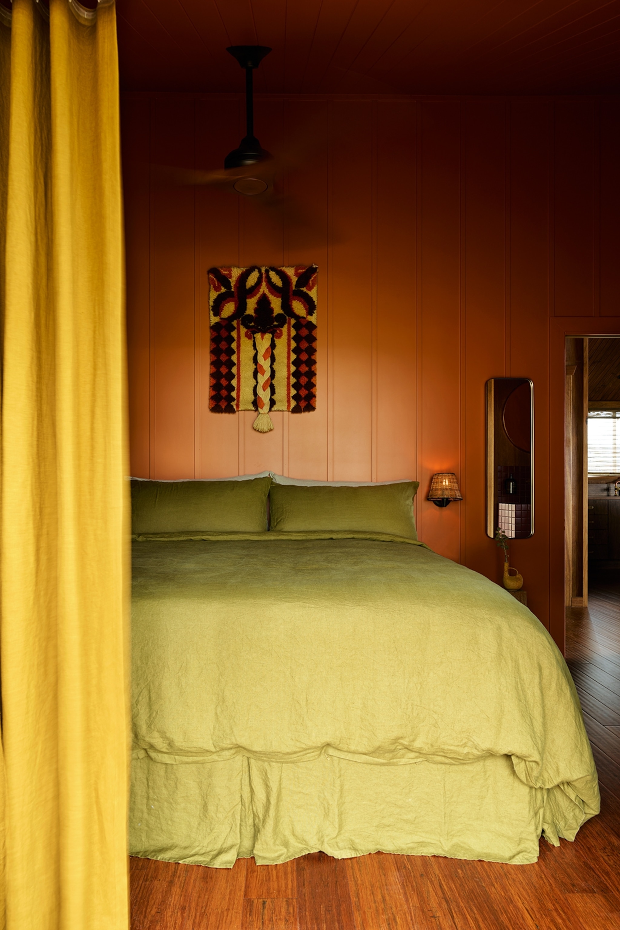 Earth toned bedroom with dark orange walls, yellow curtains and green linens