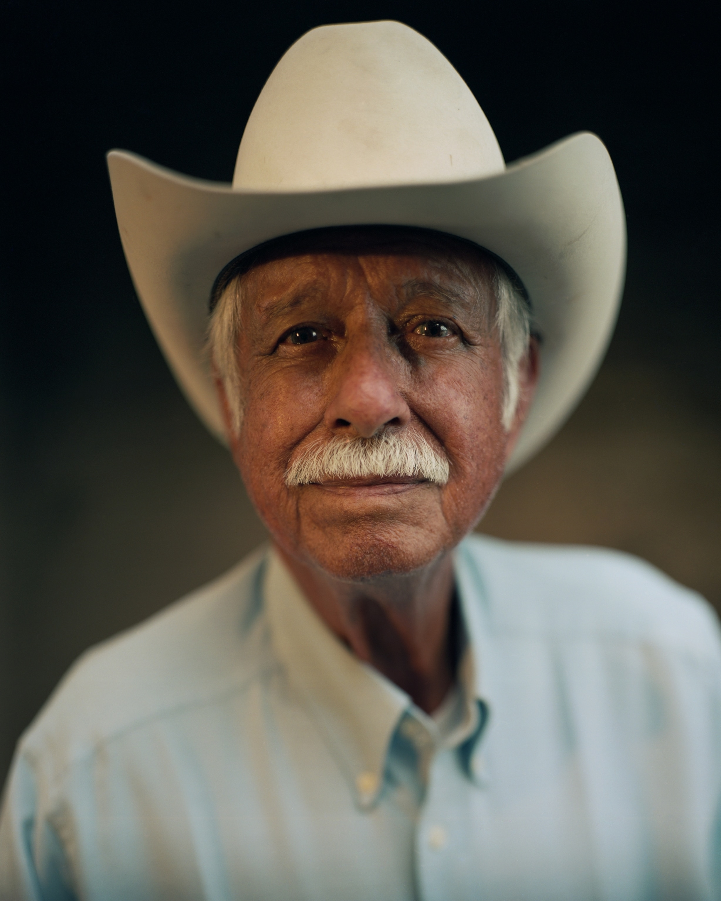 Picture of older man with grey hair and mustang in white cowboy hat.
