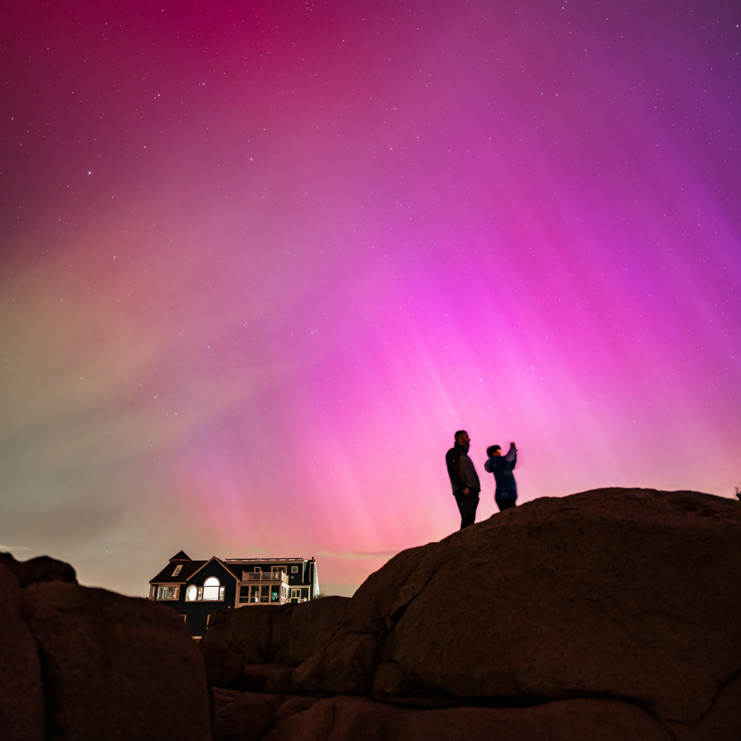 An adult and child stand silhouetted beneath a dramatic purple sky caused by the Northern Lights.