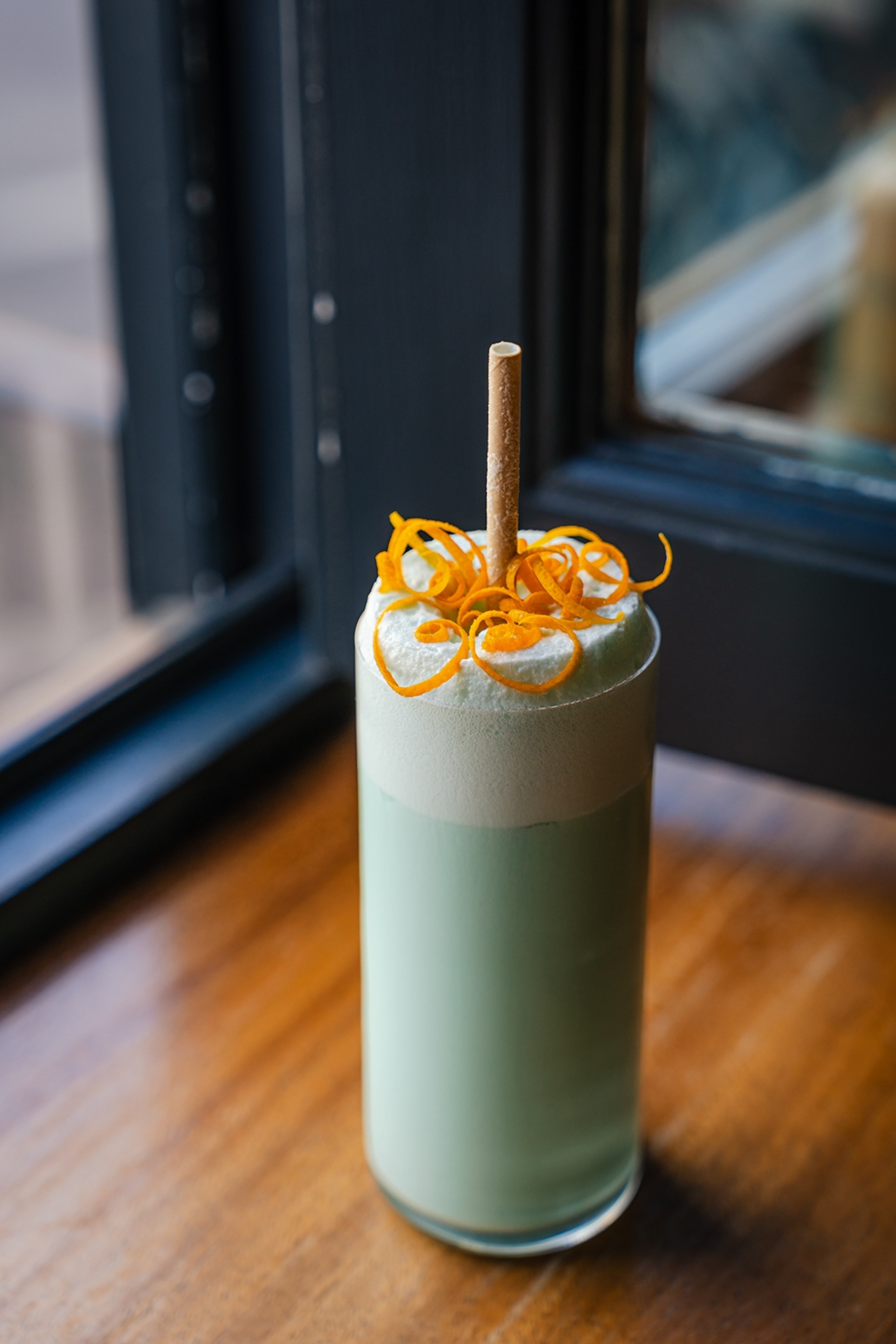 Green drink in a tall glass topped with an orange garnish