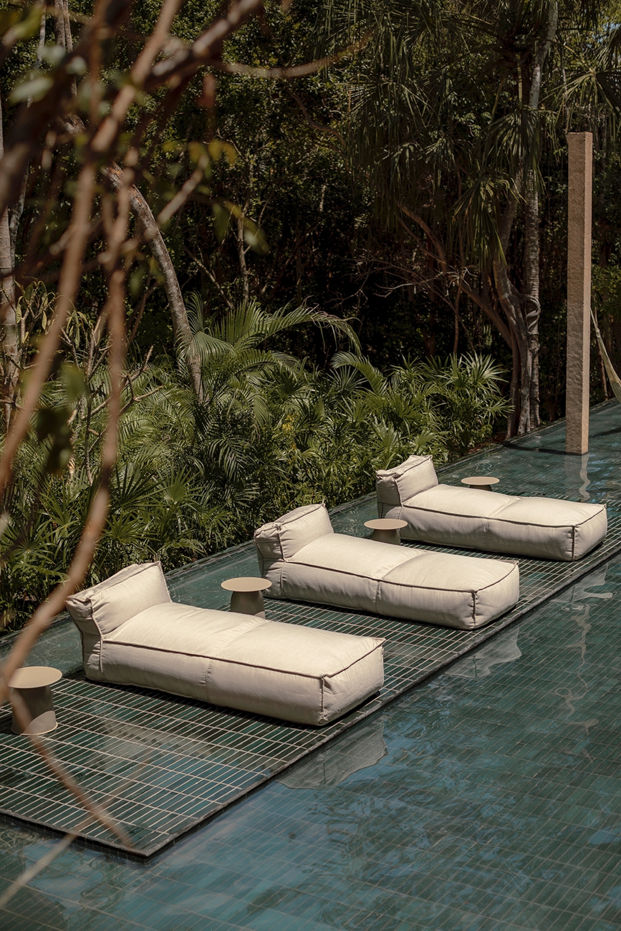 Cushioned beds positioned at the edge of a pool surrounded by jungle