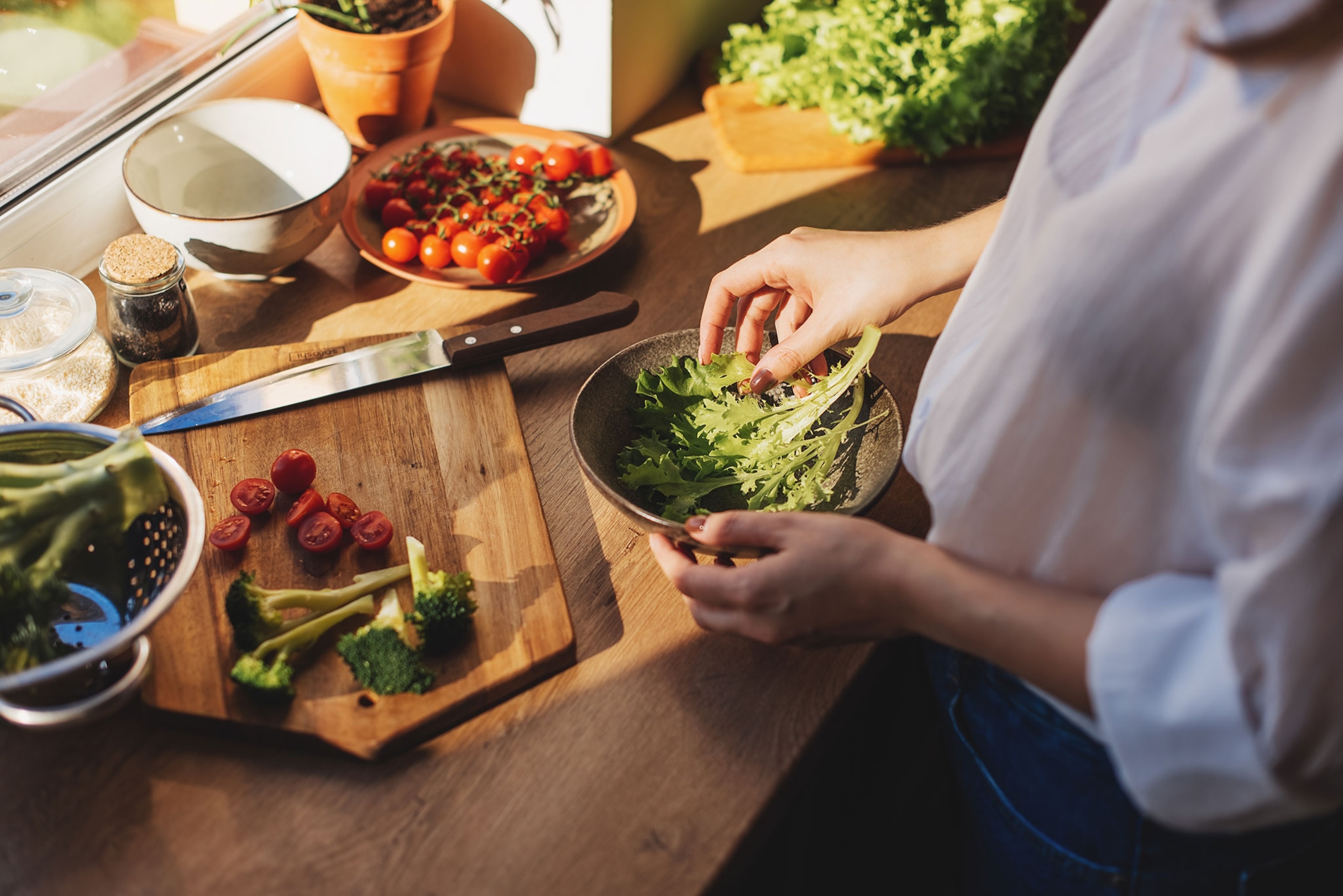 Woman in t-shirt and jeans preparing a vegan superbowl or Buddha bowl with hummus, vegetable, salad, beans, couscous and avocado