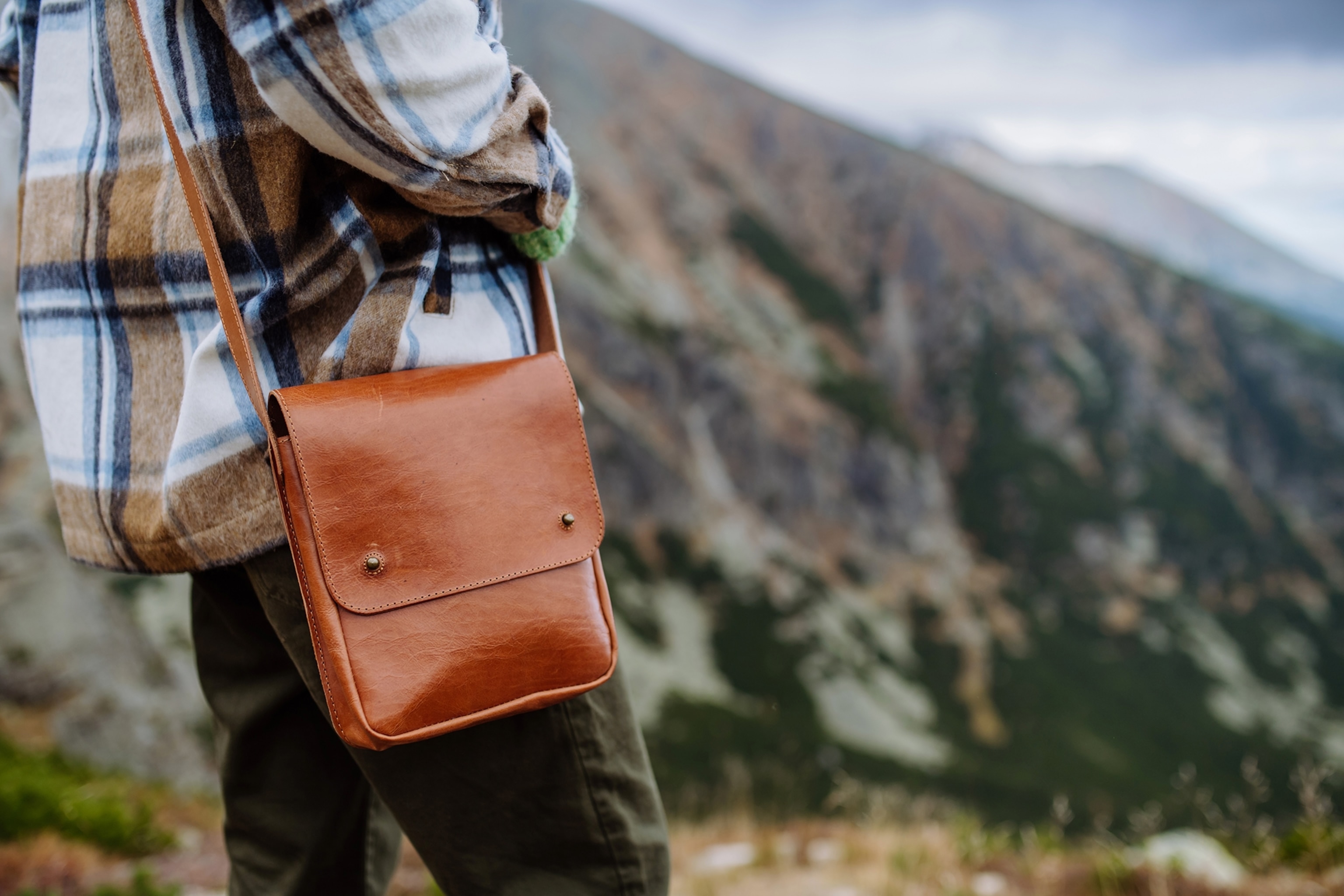 A woman with a brown bag looking at the mountains with a single strapped bag