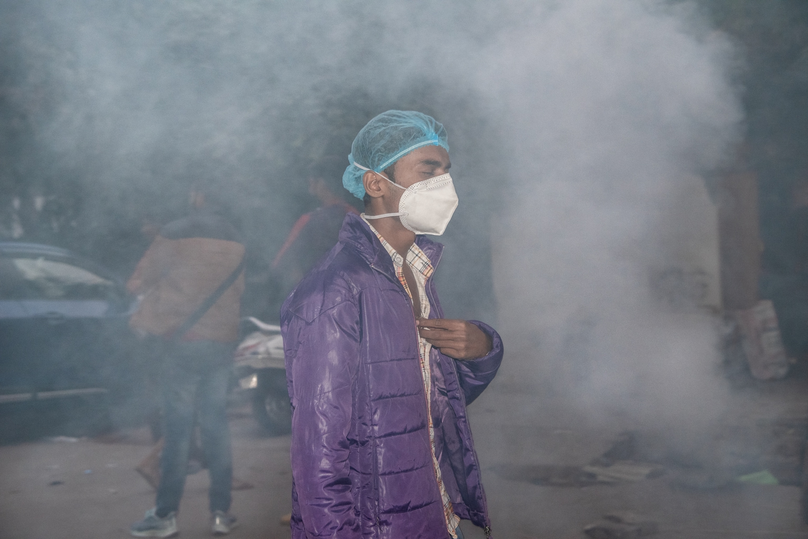 Picture of man in face mask walking through smoke from burning wood.