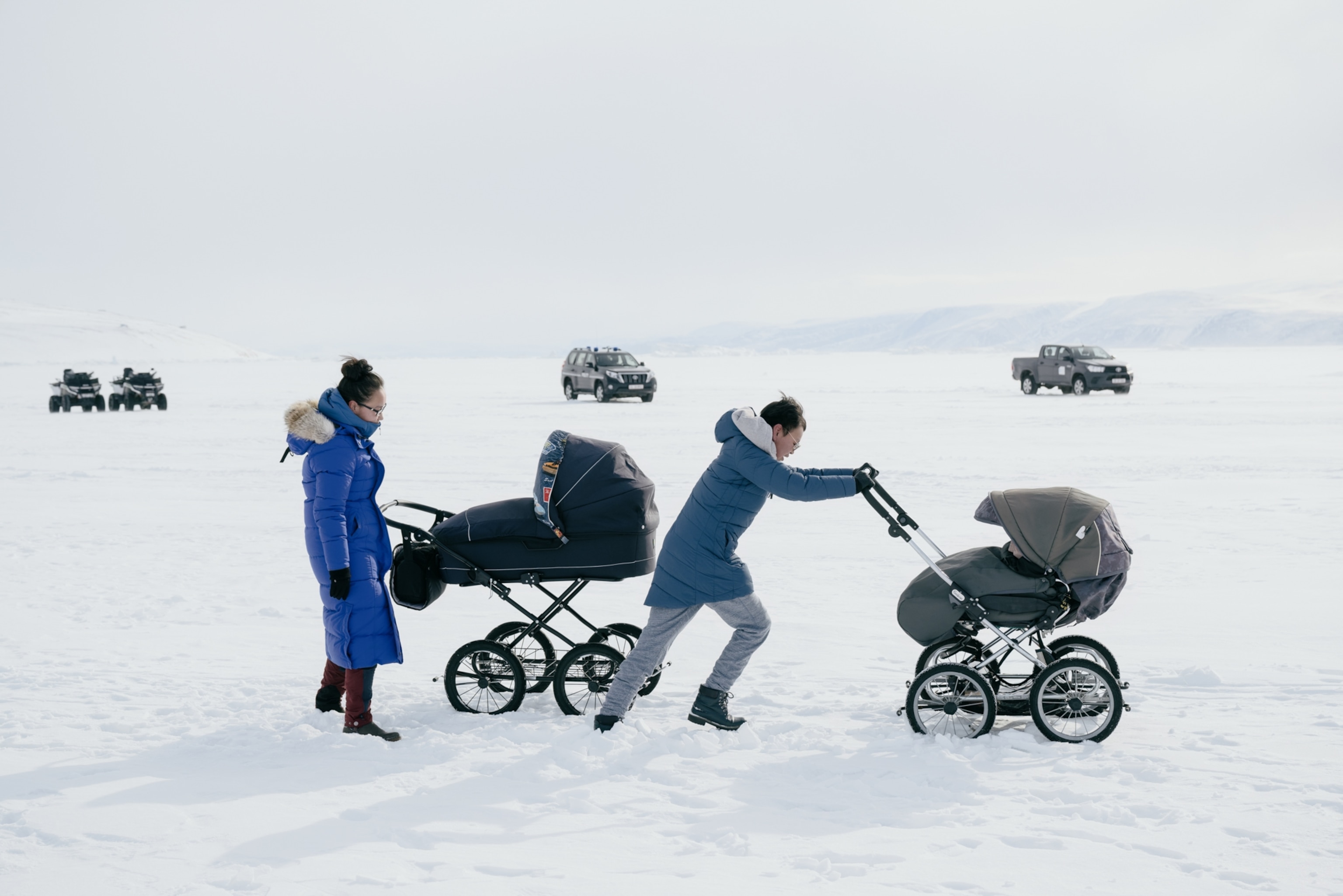 Two people pushing baby strollers across ice in the arctic