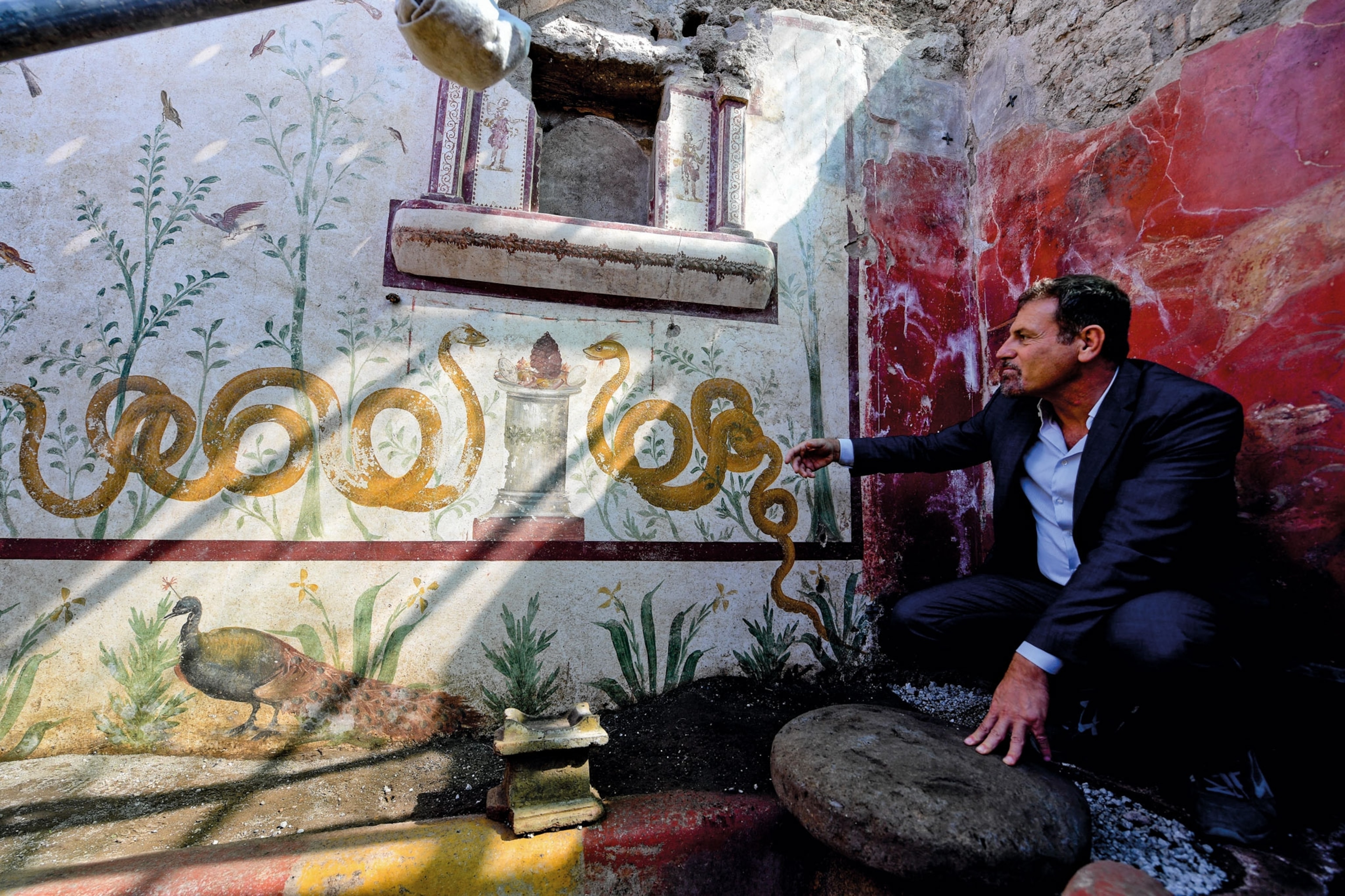 a man pointing to fresco of two snakes