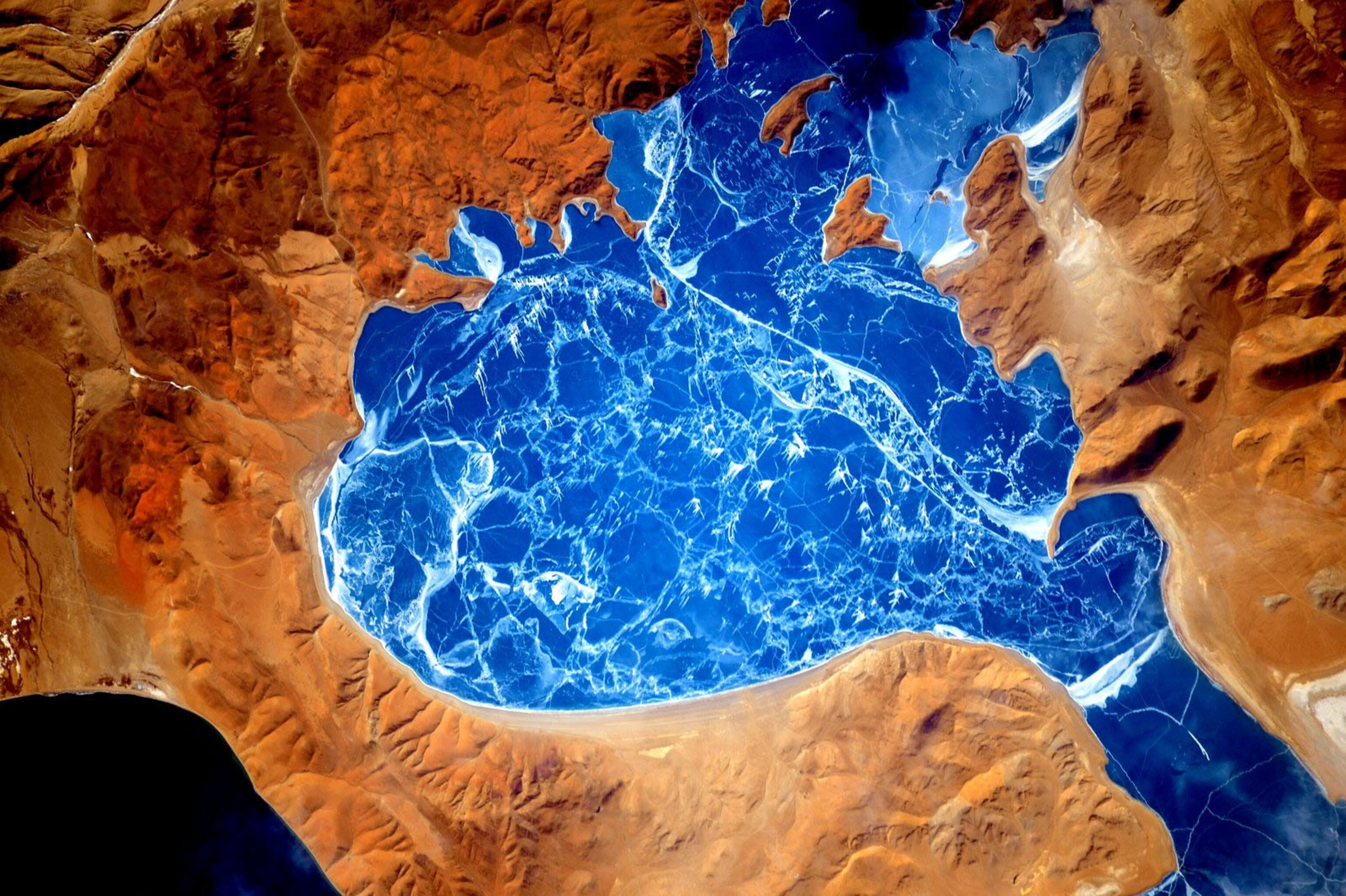 an aerial view of a rich blue lake surrounded by tan mountain
