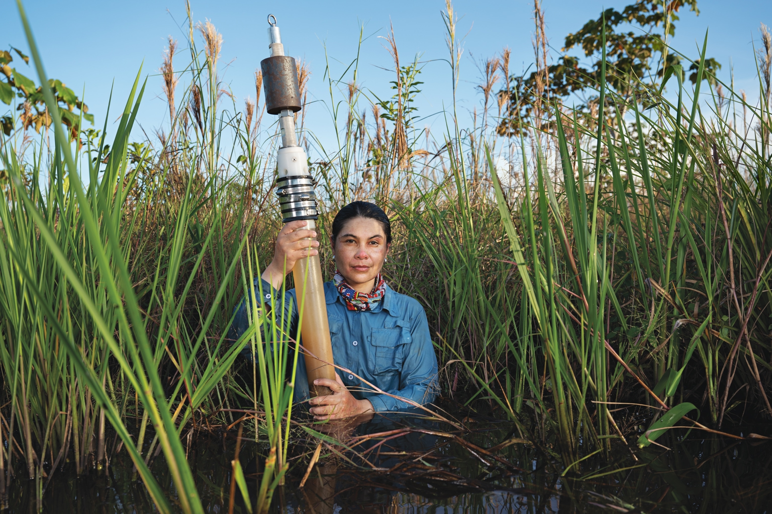 Woman standing in swamp water up to her waist and holding a pipe.