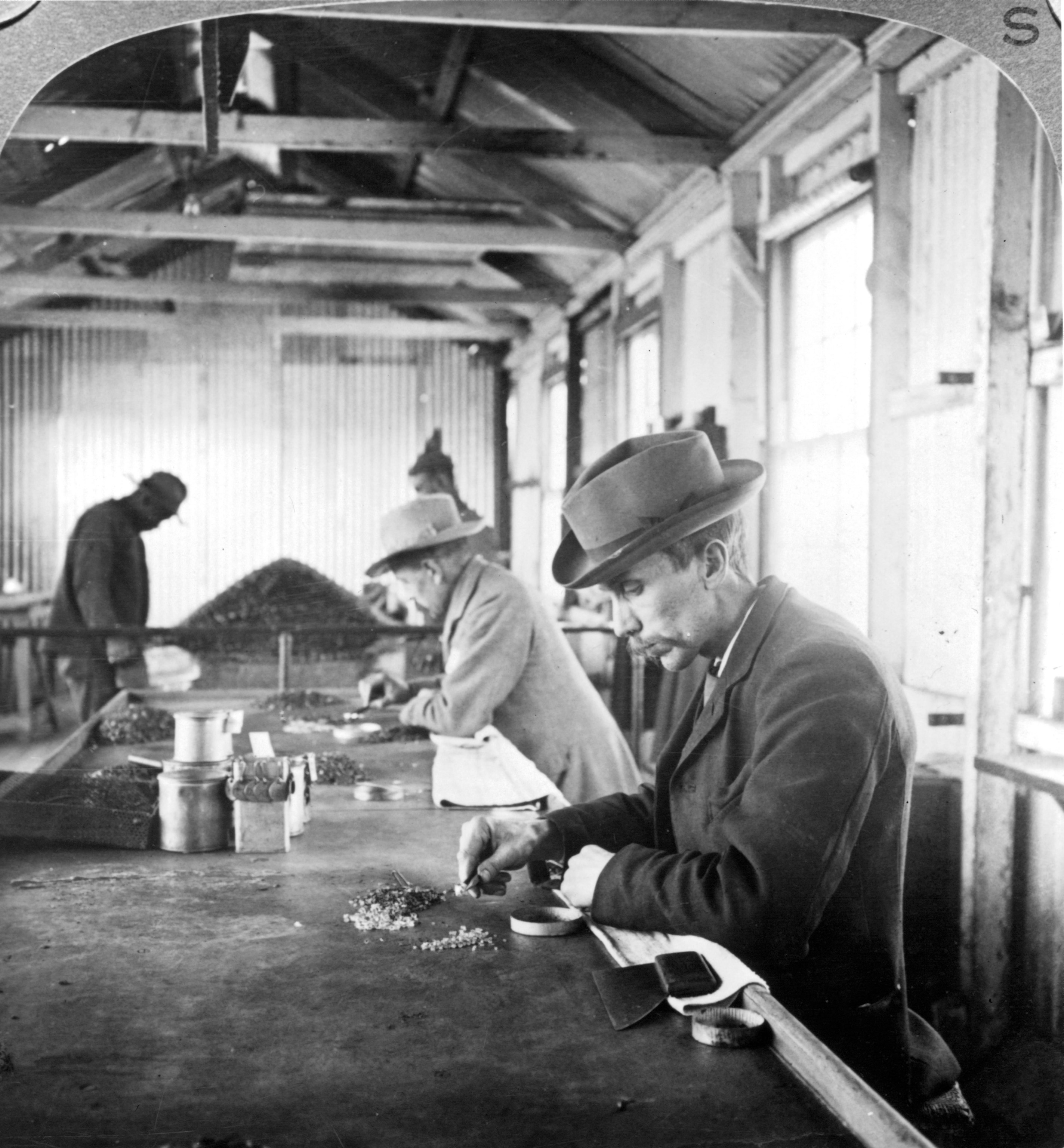 a black and white photo of workers sorting through diamonds