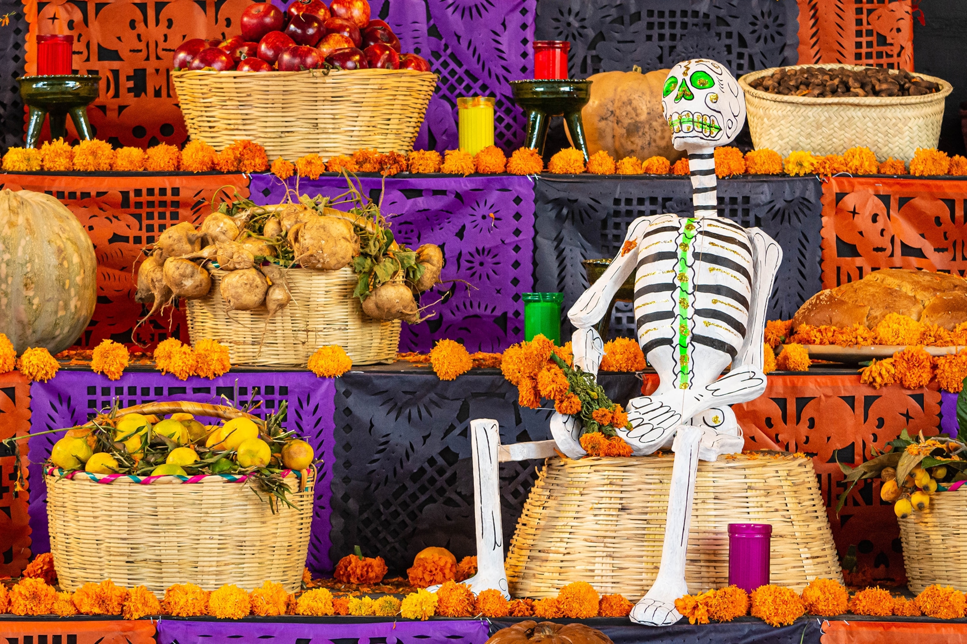 A close up of a decorated, tiered altar with flowers and a sitting skeleton in the corner.