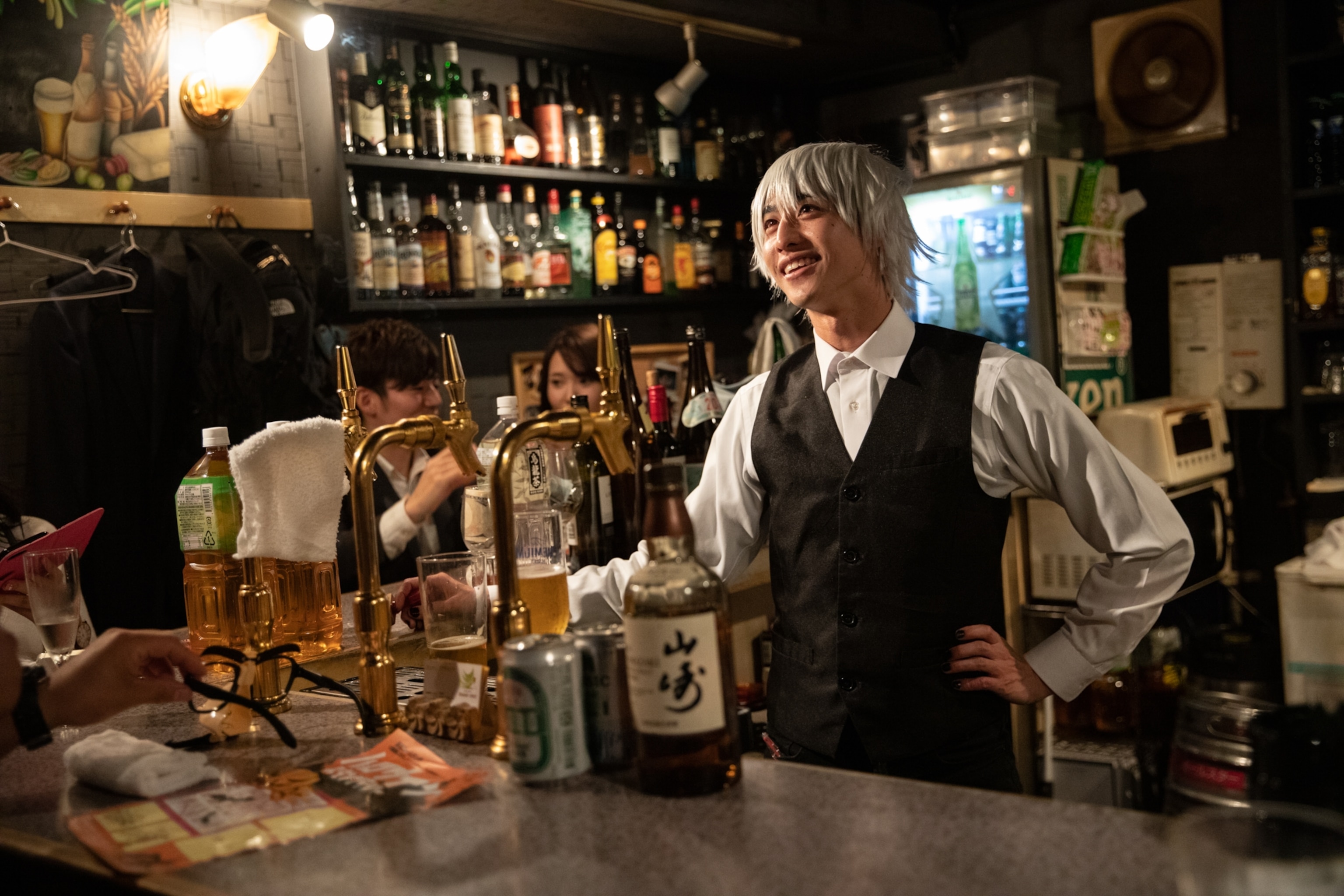 A guy with a short wig and a black vest and white button down shirt.