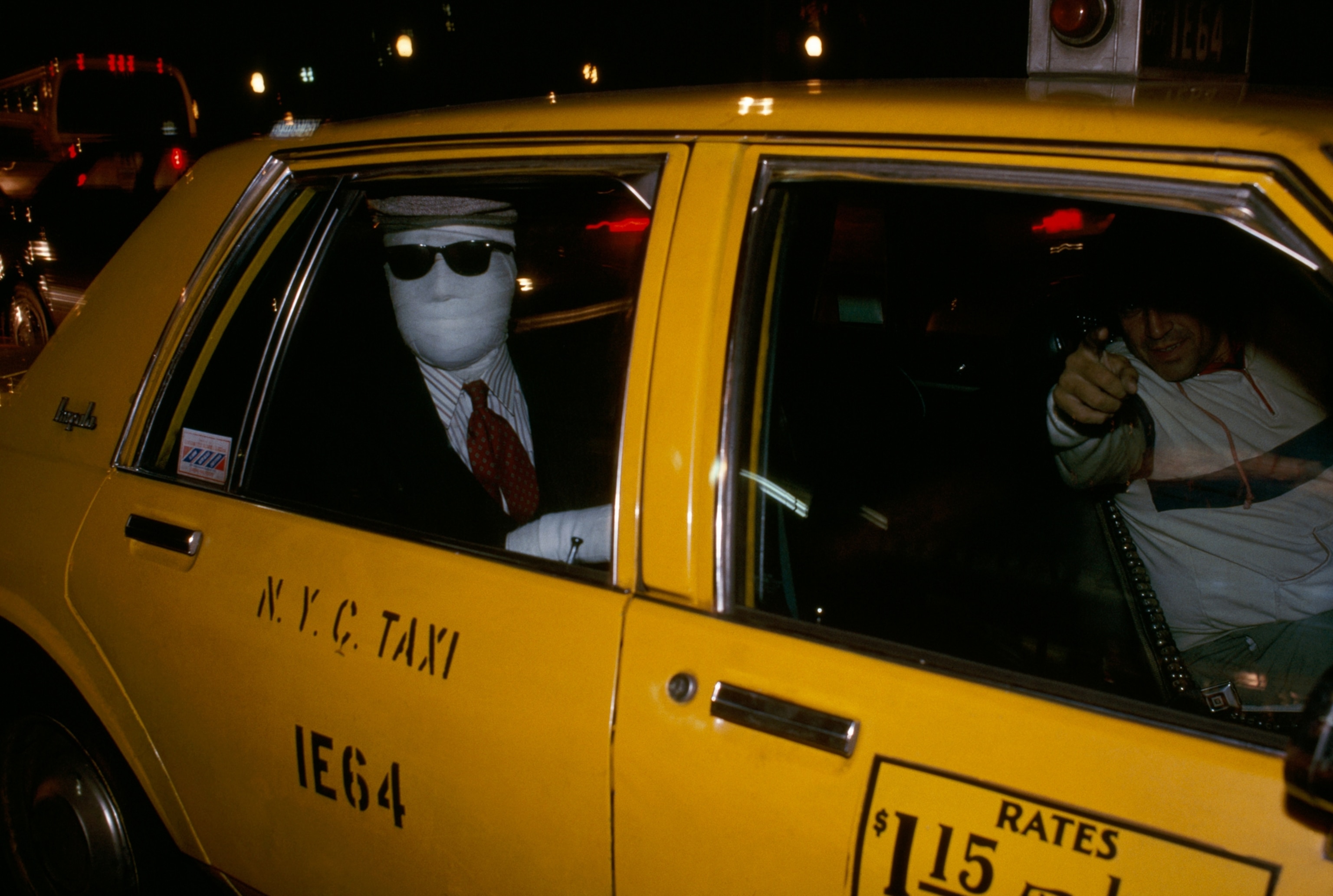 A man wrapped in gauze as part of a costume sits in the back of a taxi on Halloween