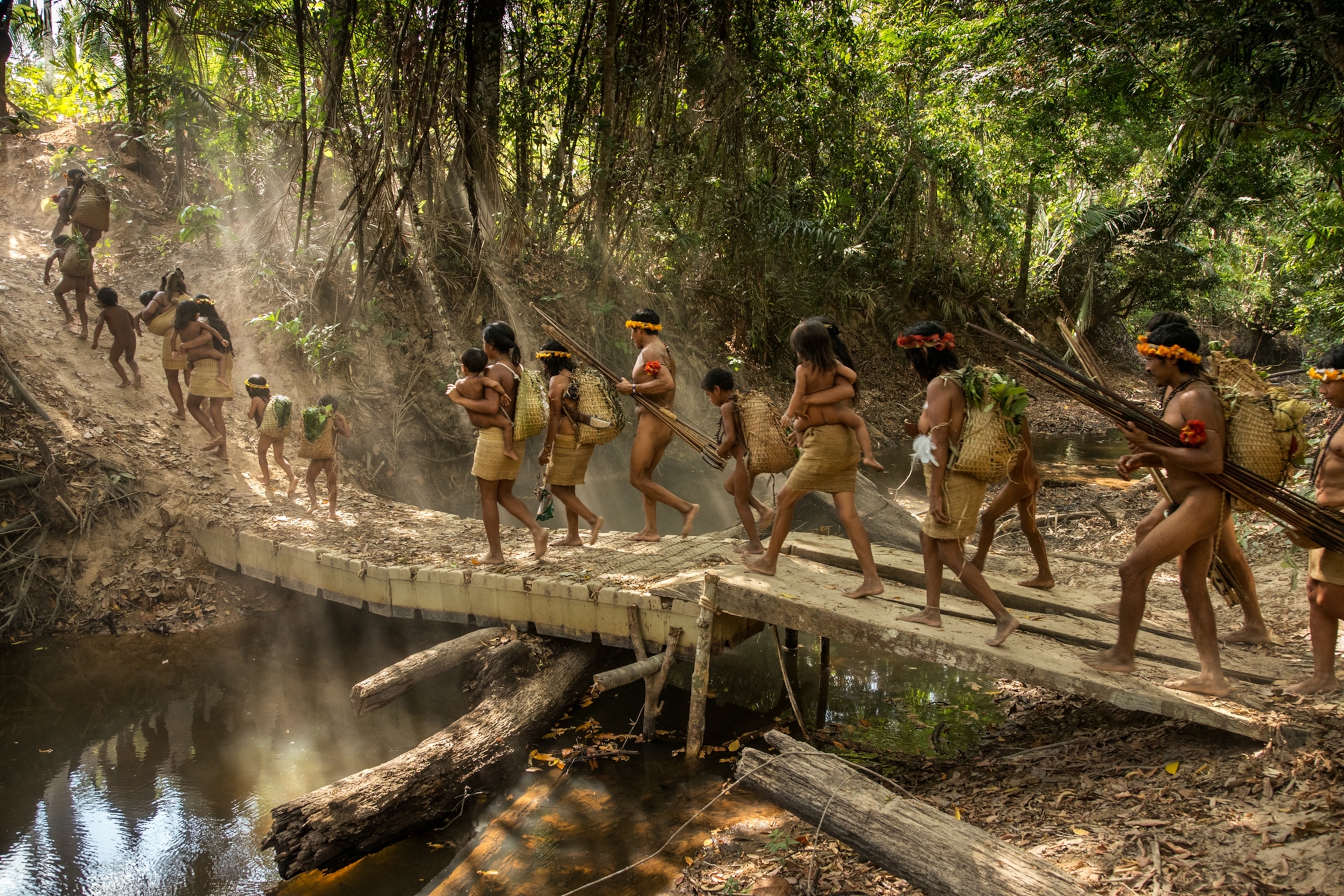 a family of adults and young children walking across a bridge into a forest