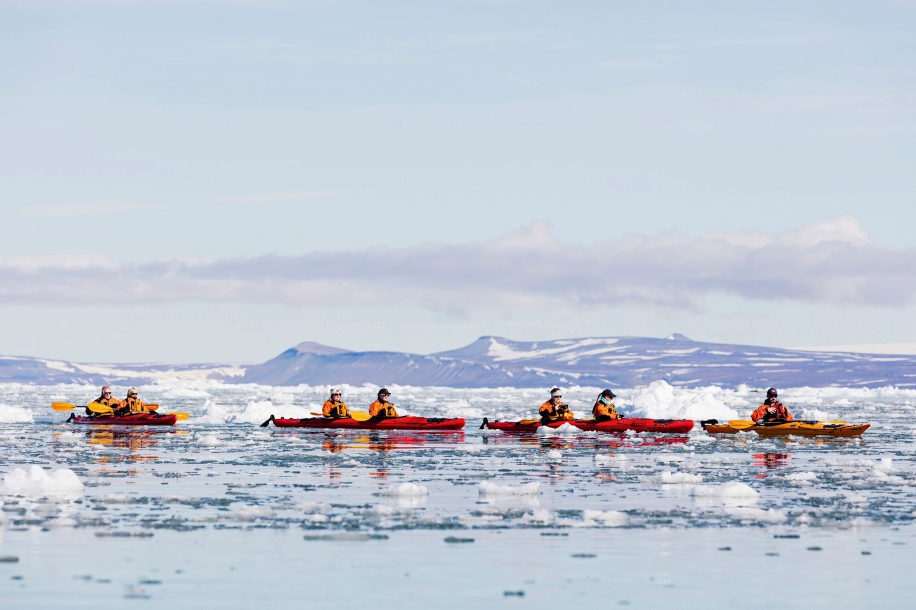 People kayaking across an iceberg filled glacial lagoon.