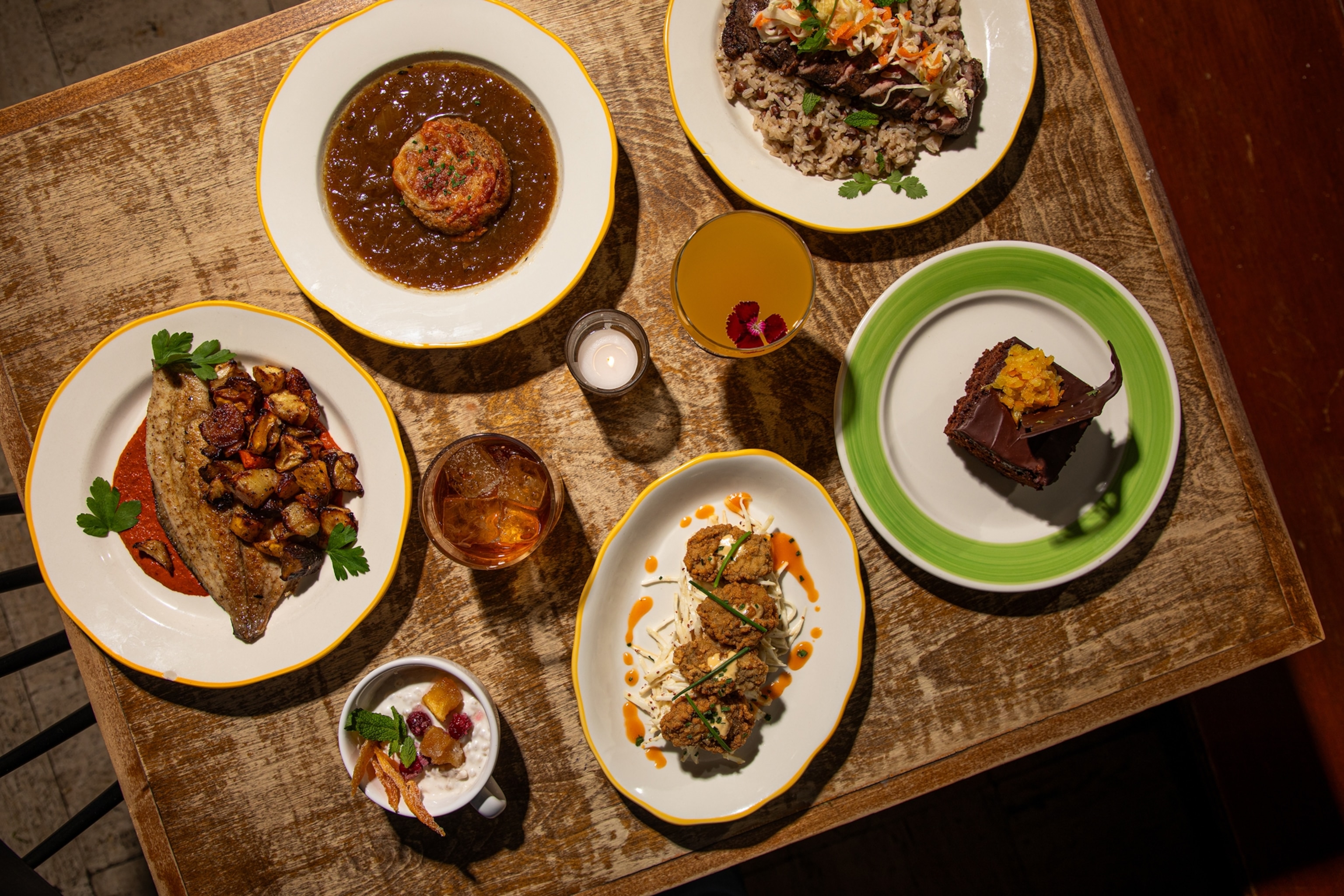 An overhead view of plated entrees, appetizers, desserts, and alcoholic drinks on a wooden table.