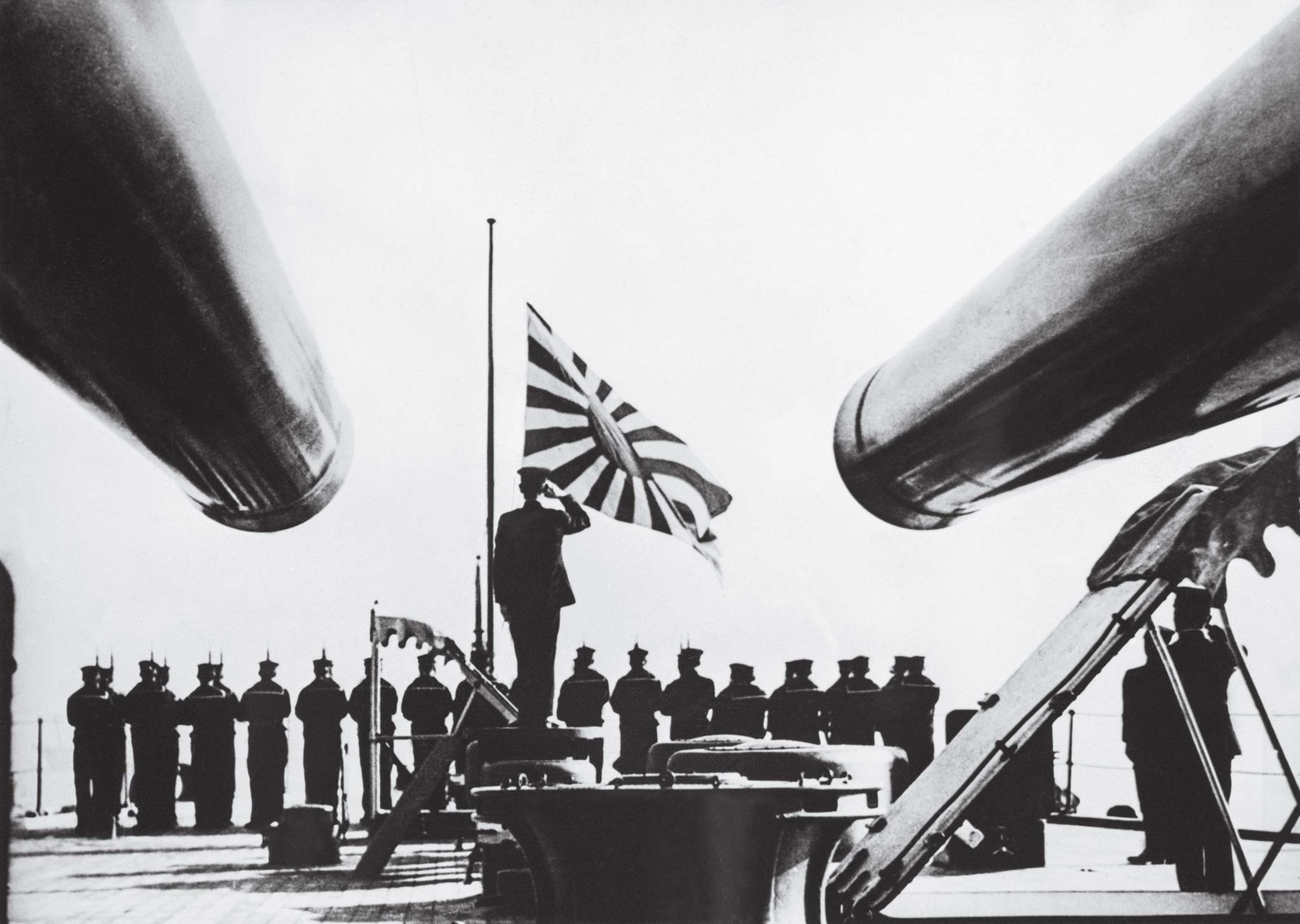 Officers and crew on a warship of the Imperial Japanese Navy salute their flag, emblazoned with the rising sun.