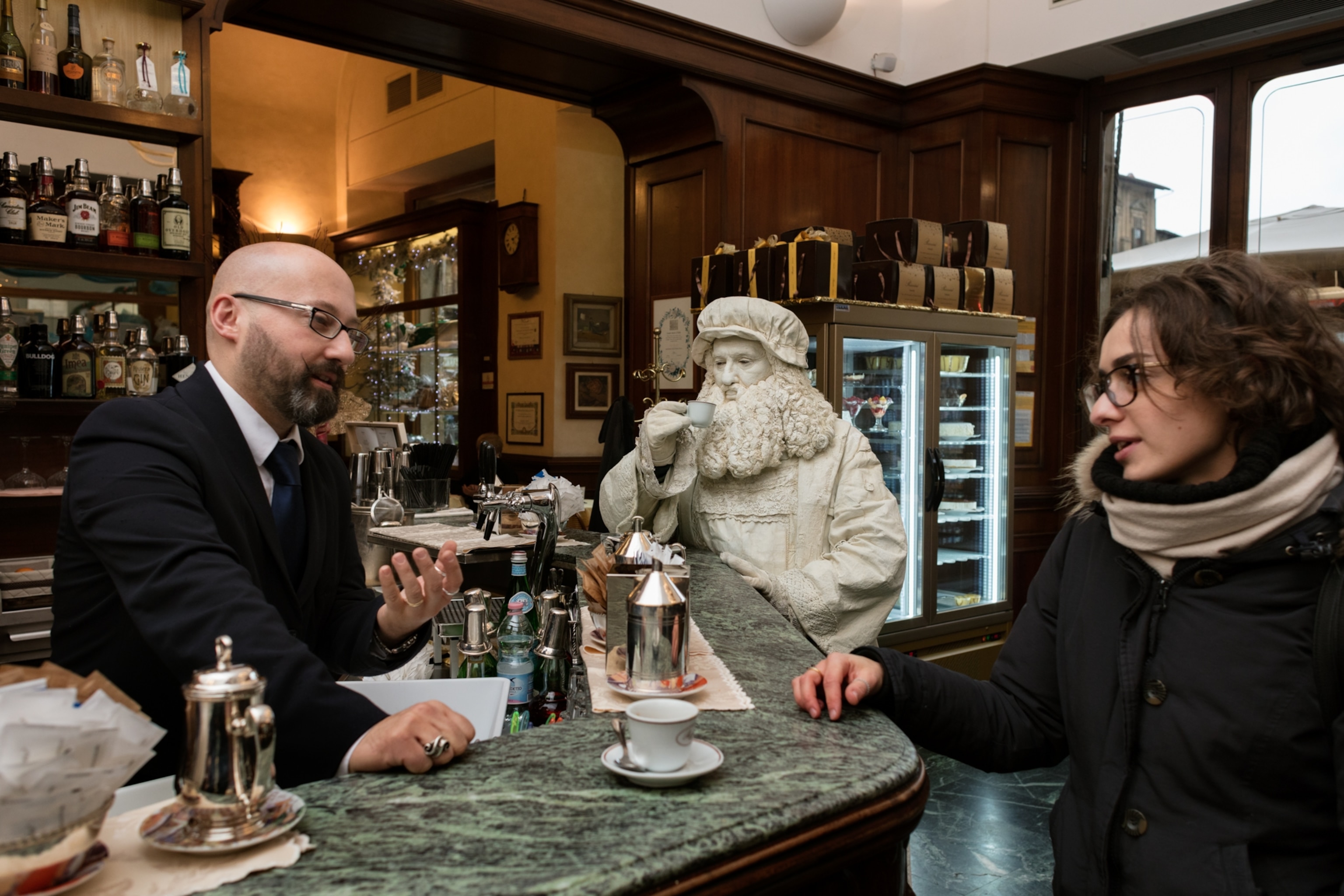 an medieval impersonator in all white at a cafe sipping espresso flanked by two people