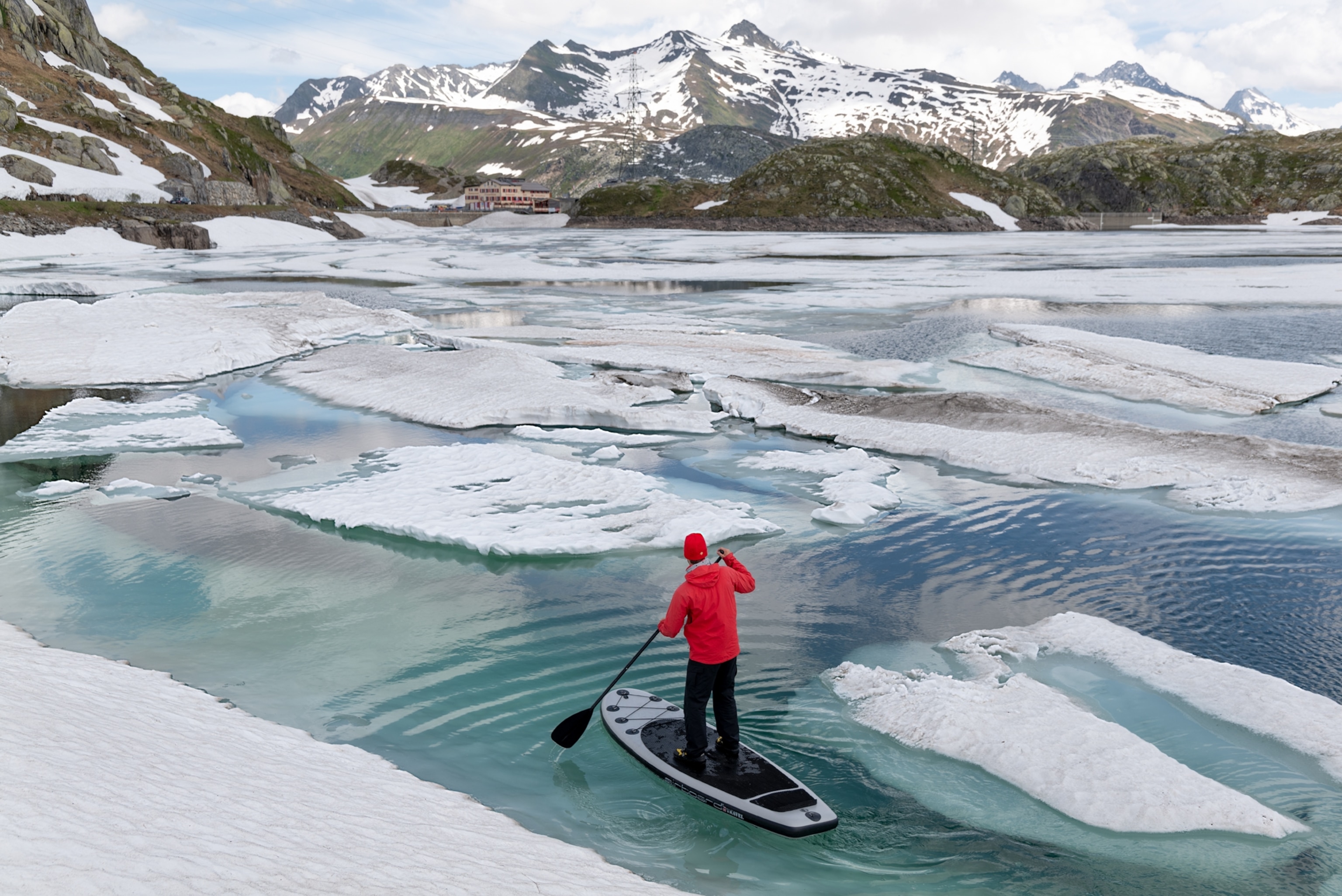 Picture of man in red jacket and red heat on paddle-board navigation through ice.