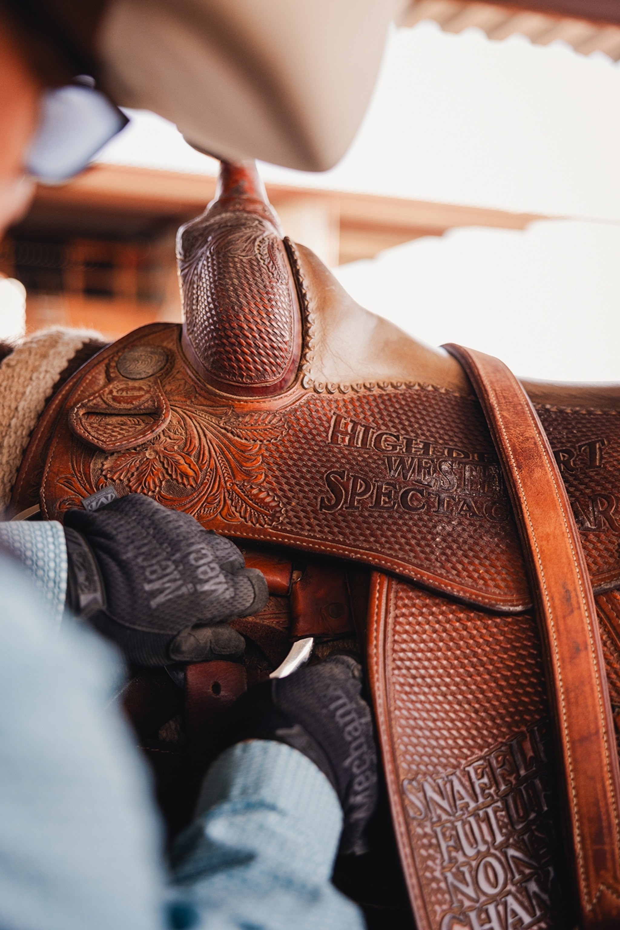 A close-shot of a mans hands saddling his horse, preparing to ride.
