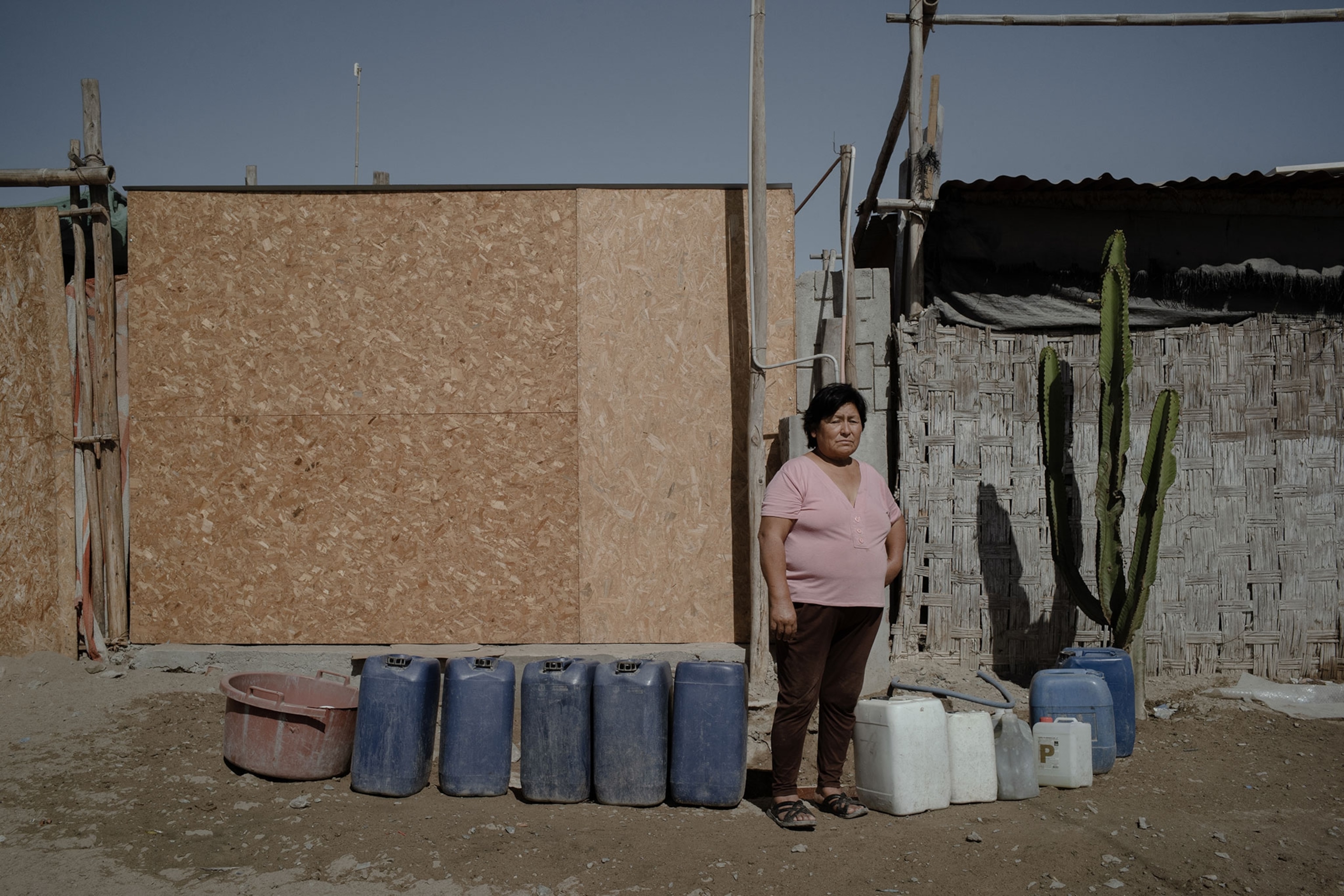 A woman standing next to water containers in front of housing structures.