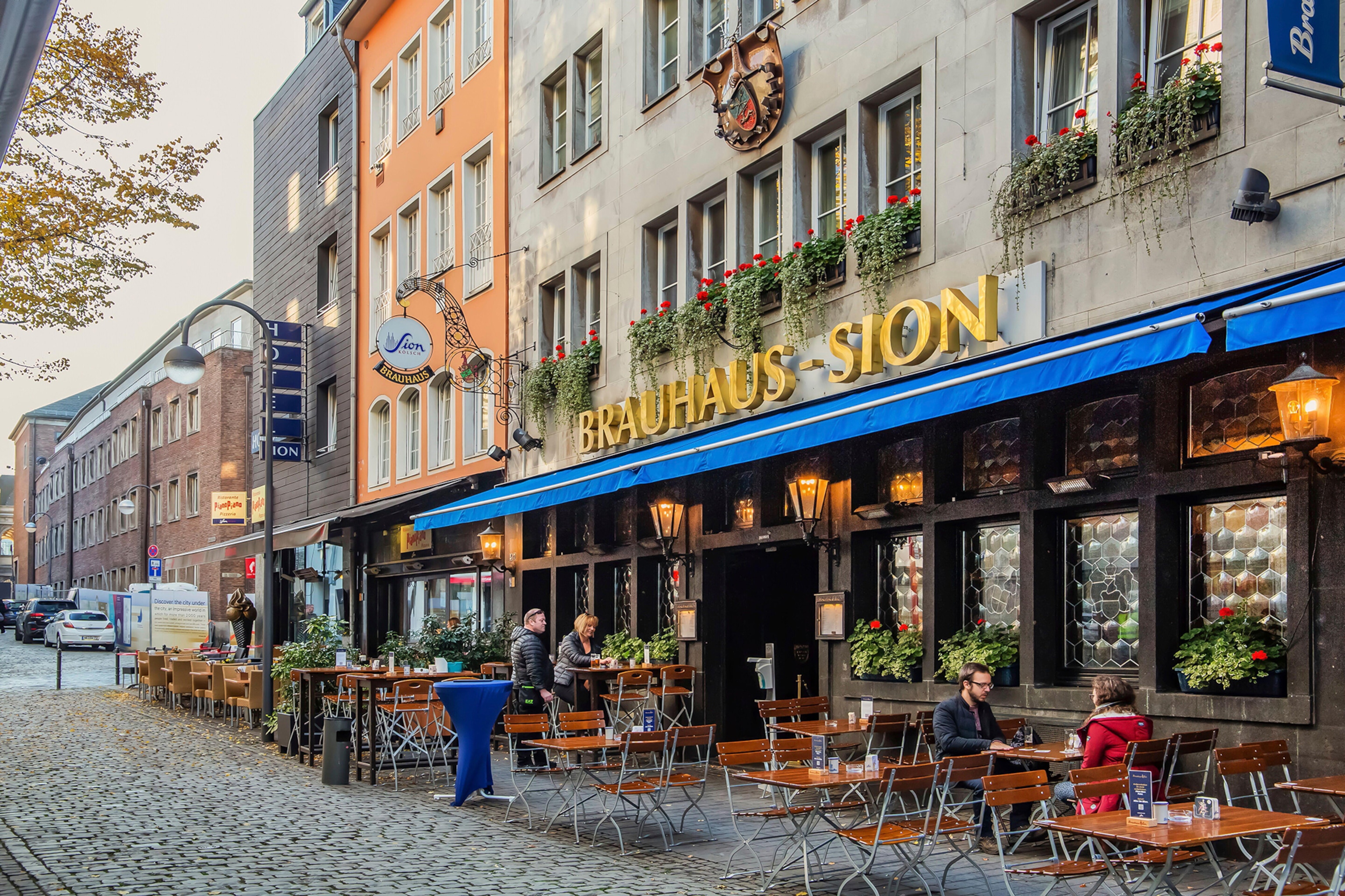 Exterior of a pub on a cobbled street with wooden tables lined up outside