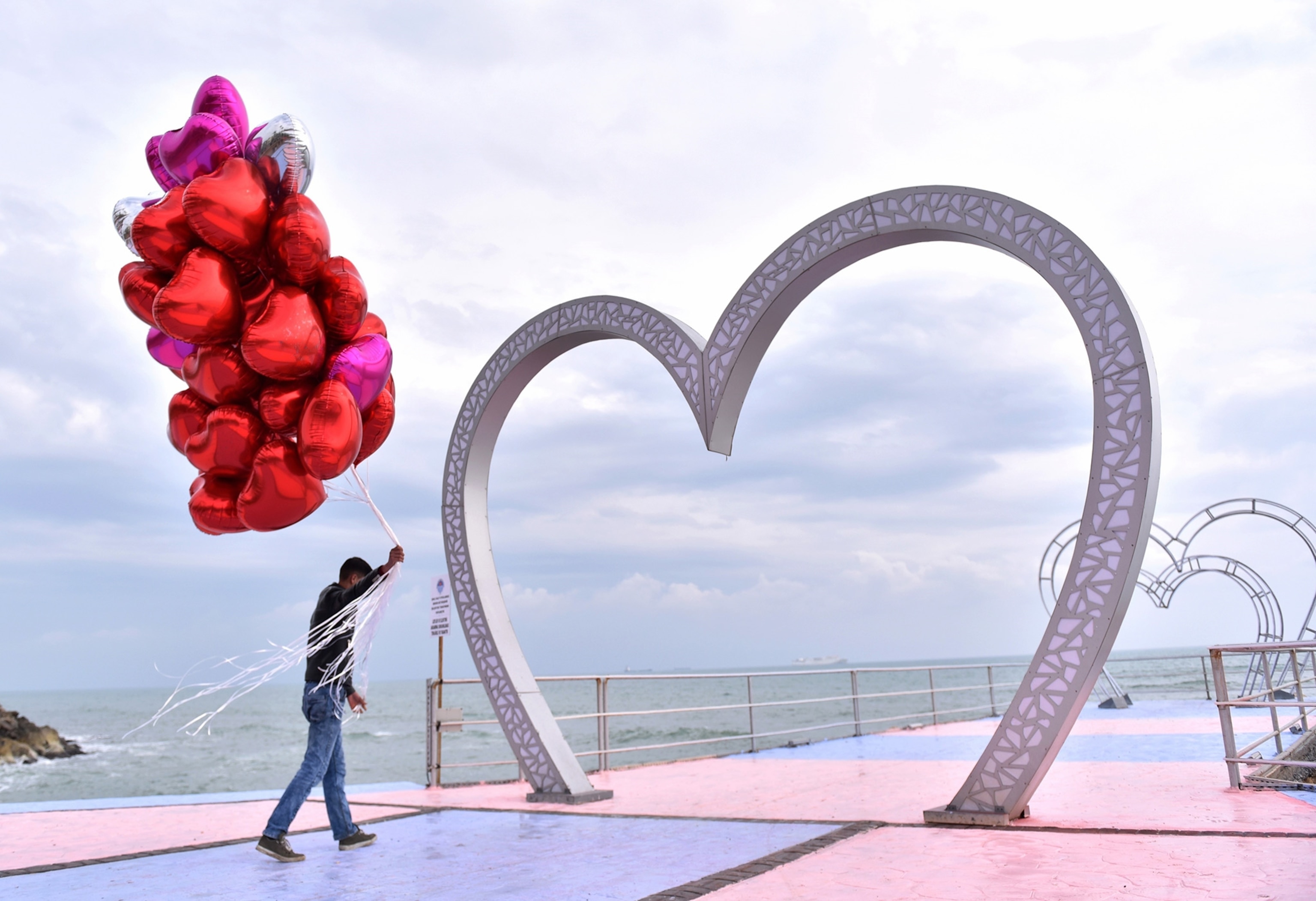A vendor walking under a heart shaped figure, with balloons in hand.