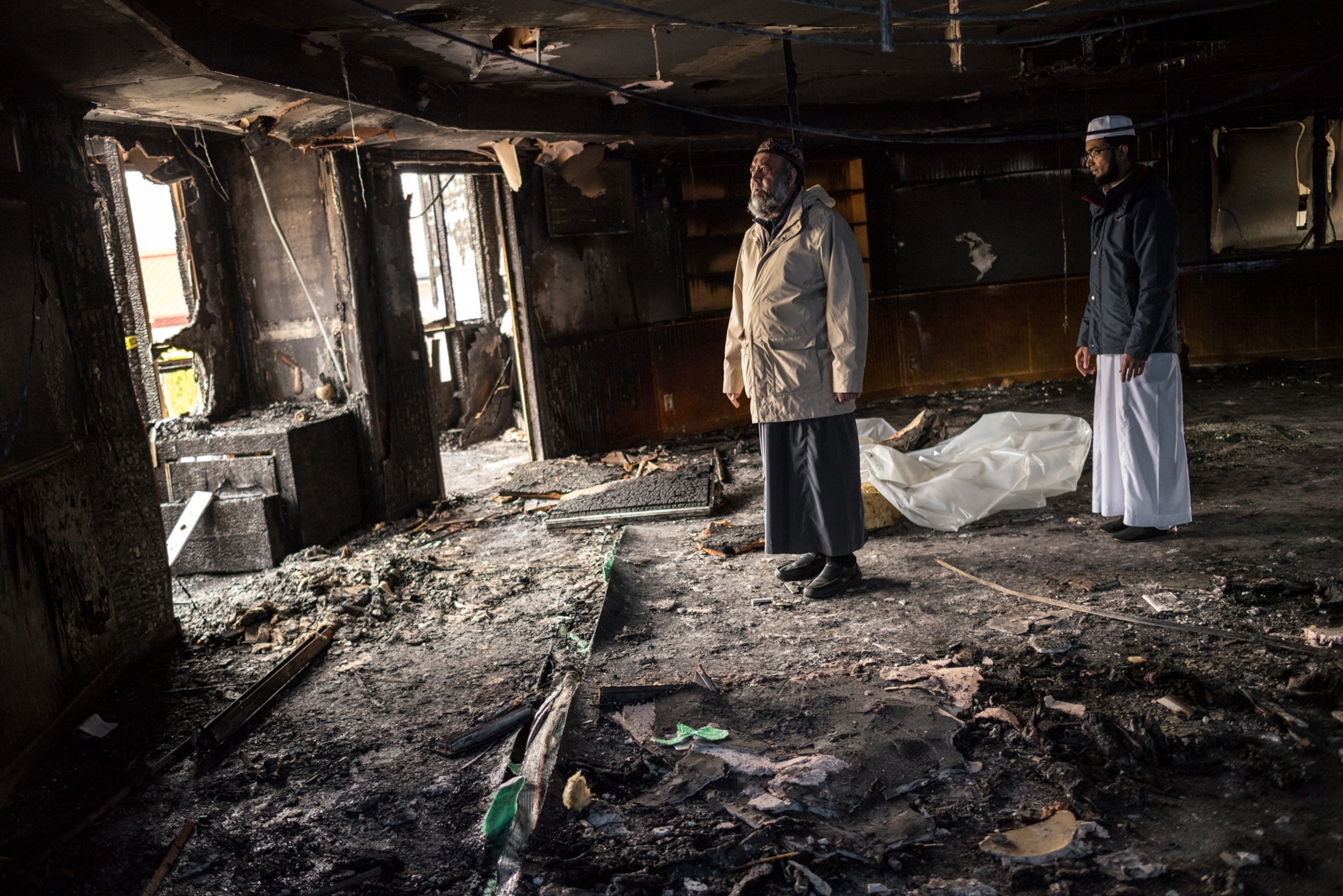 an Imam and another man standing inside a mosque that was burned