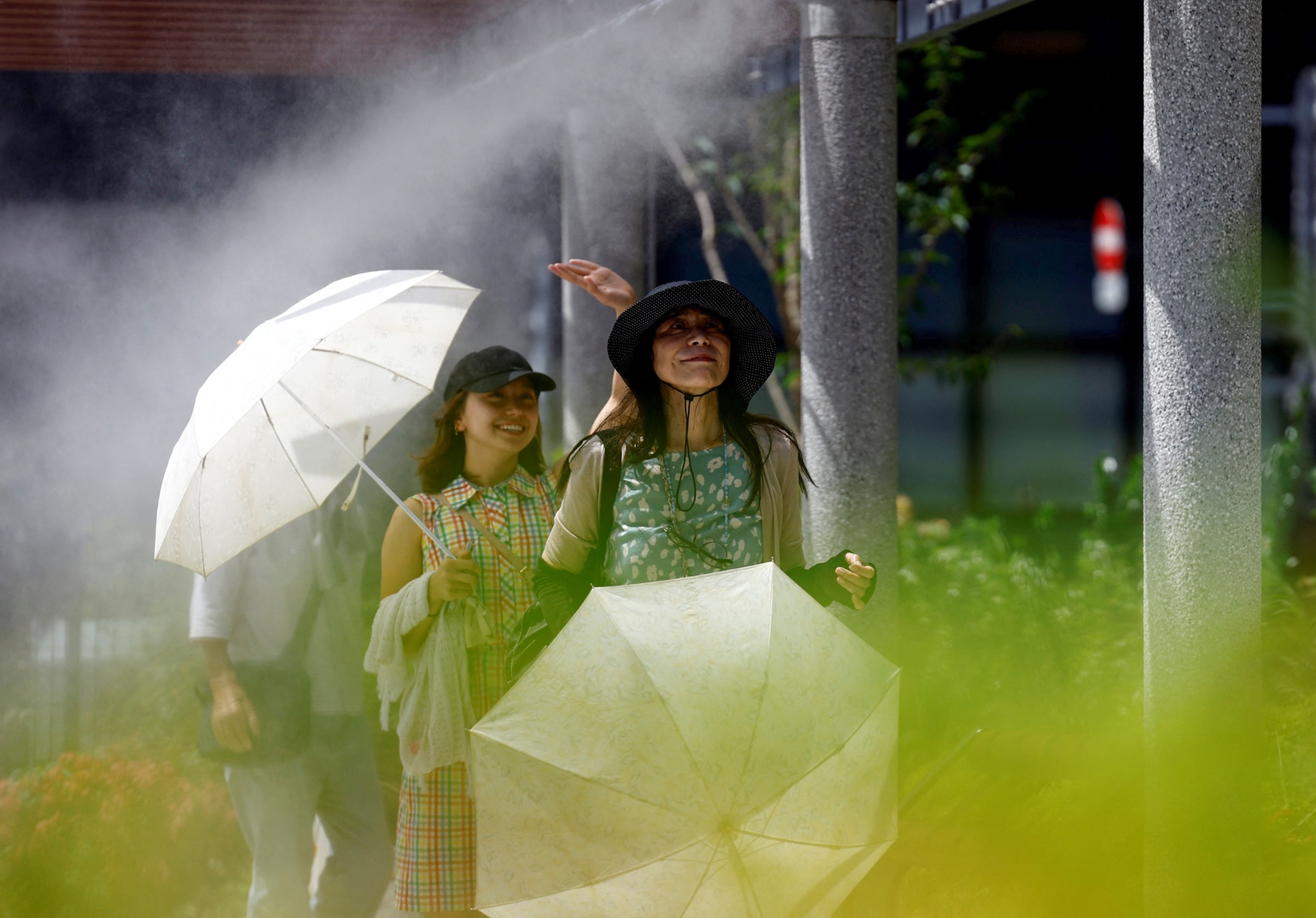 Two women carrying parasols as they walk through misters during a heatwave in Japan.