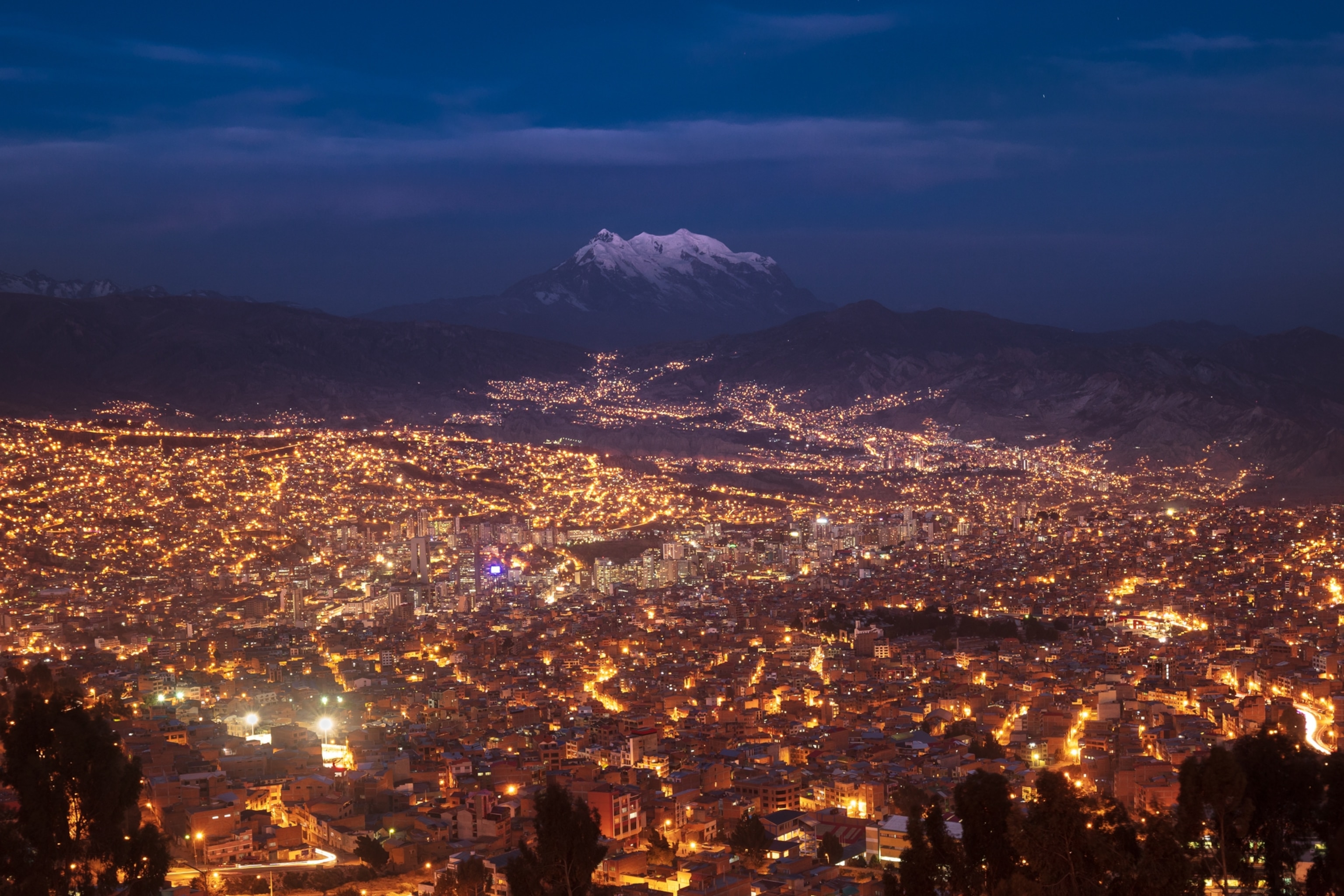 The city lights of La Paz illuminate the area, with the imposing Nevado Illimani in the background.
