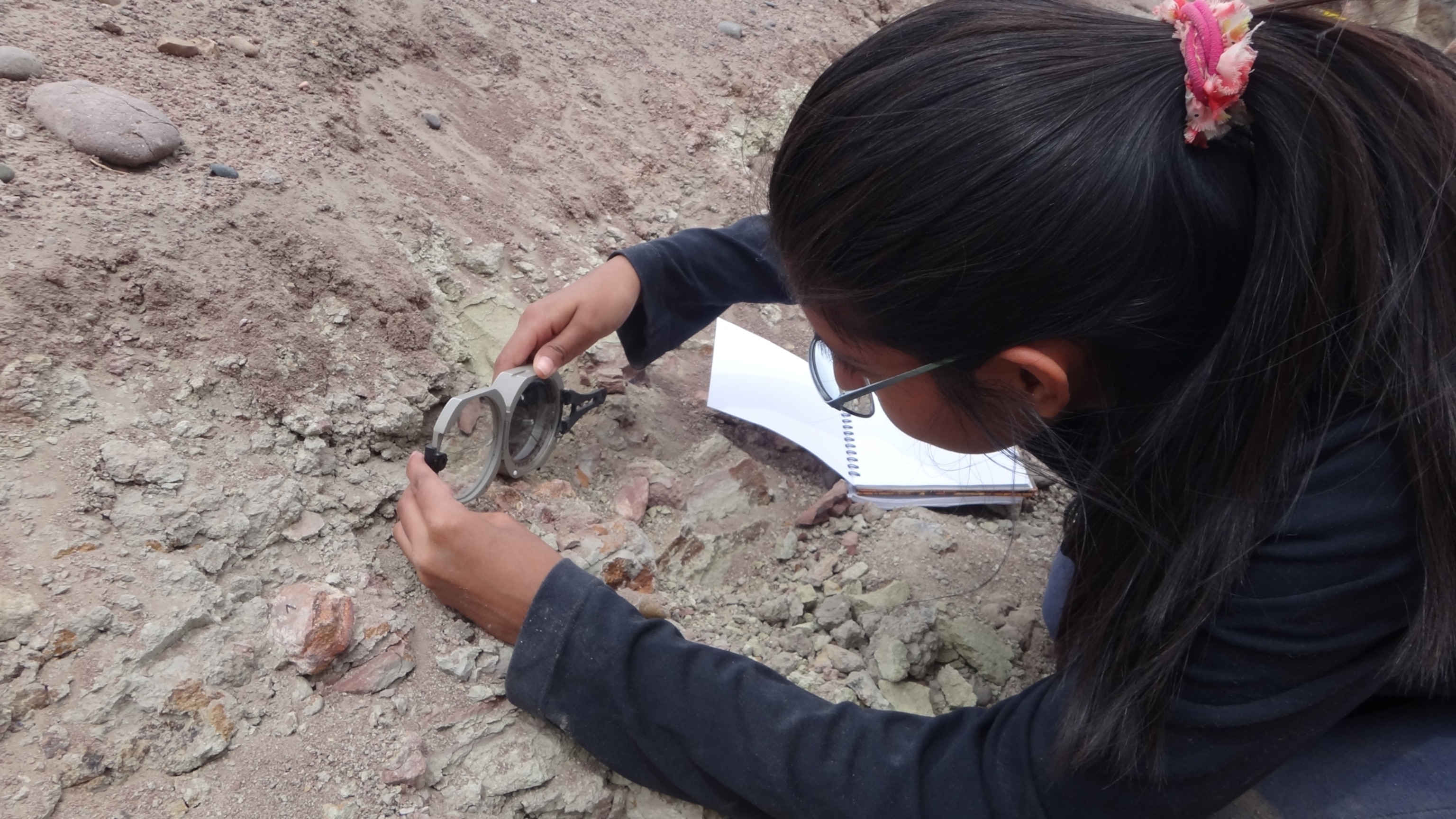 A graduate student using a compass to measure the orientation of fossils embedded in rock.