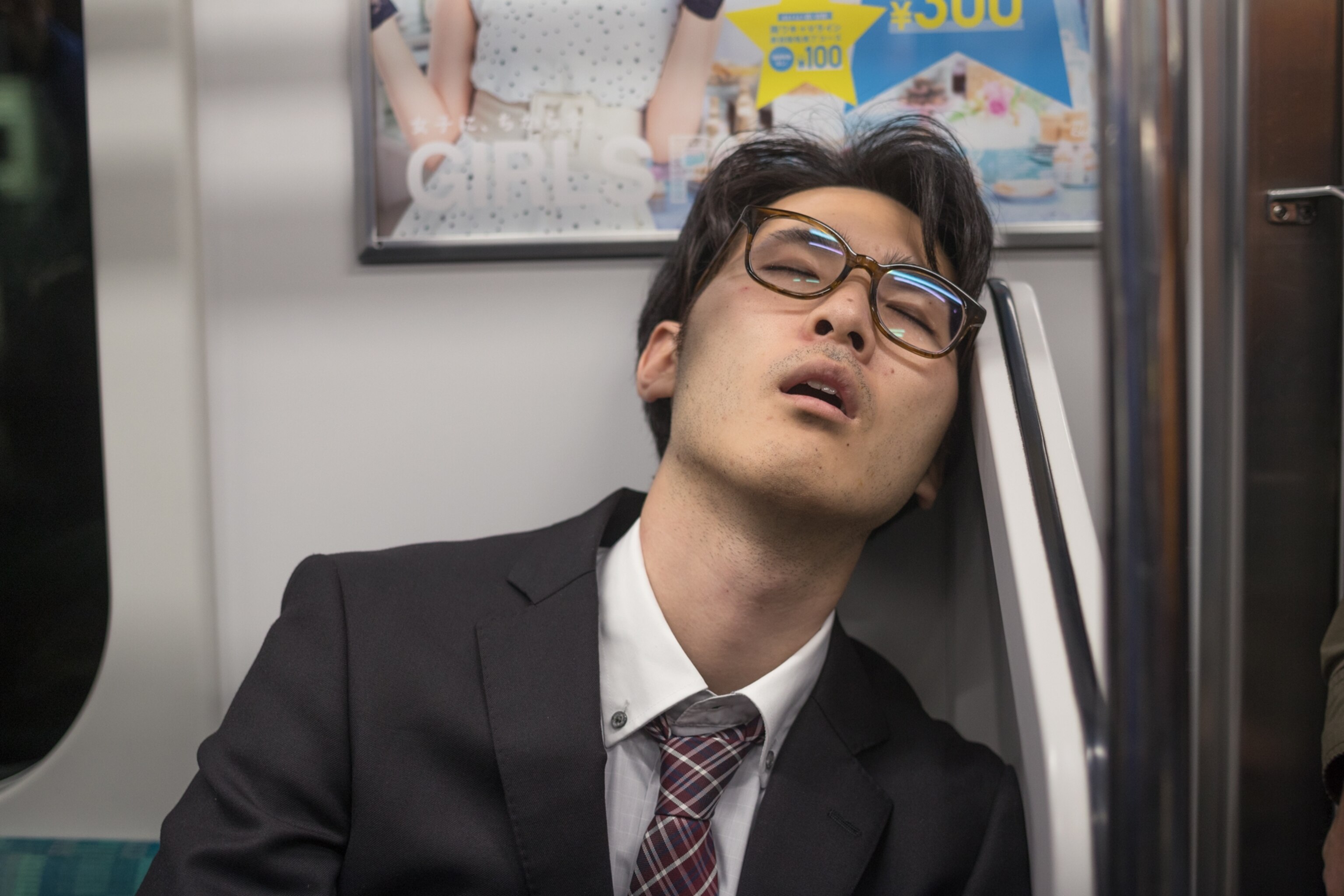 a man with glasses sleeping on a subway in Tokyo
