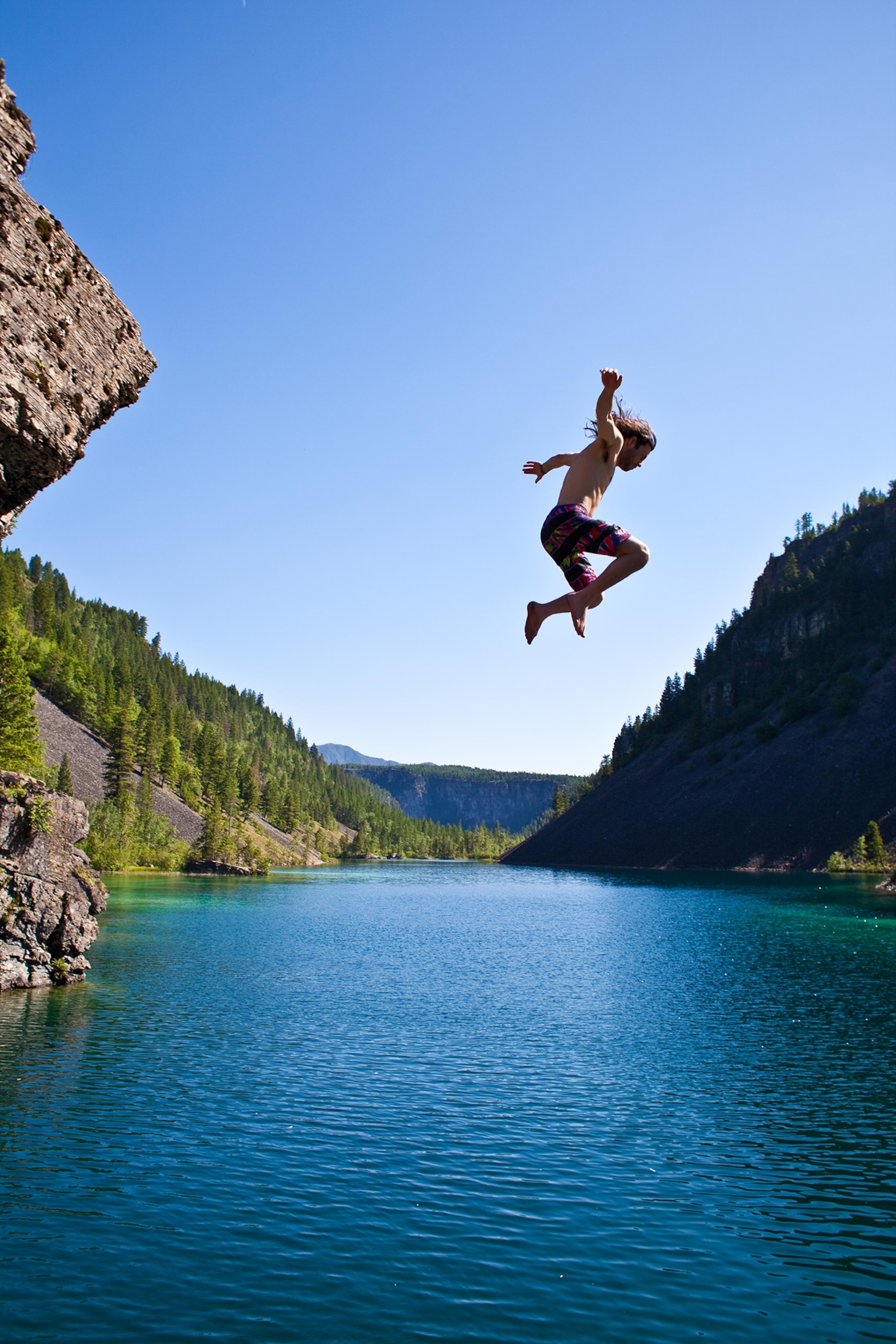 A young man cliff jumping near Fernie, BC on scorching summer day.