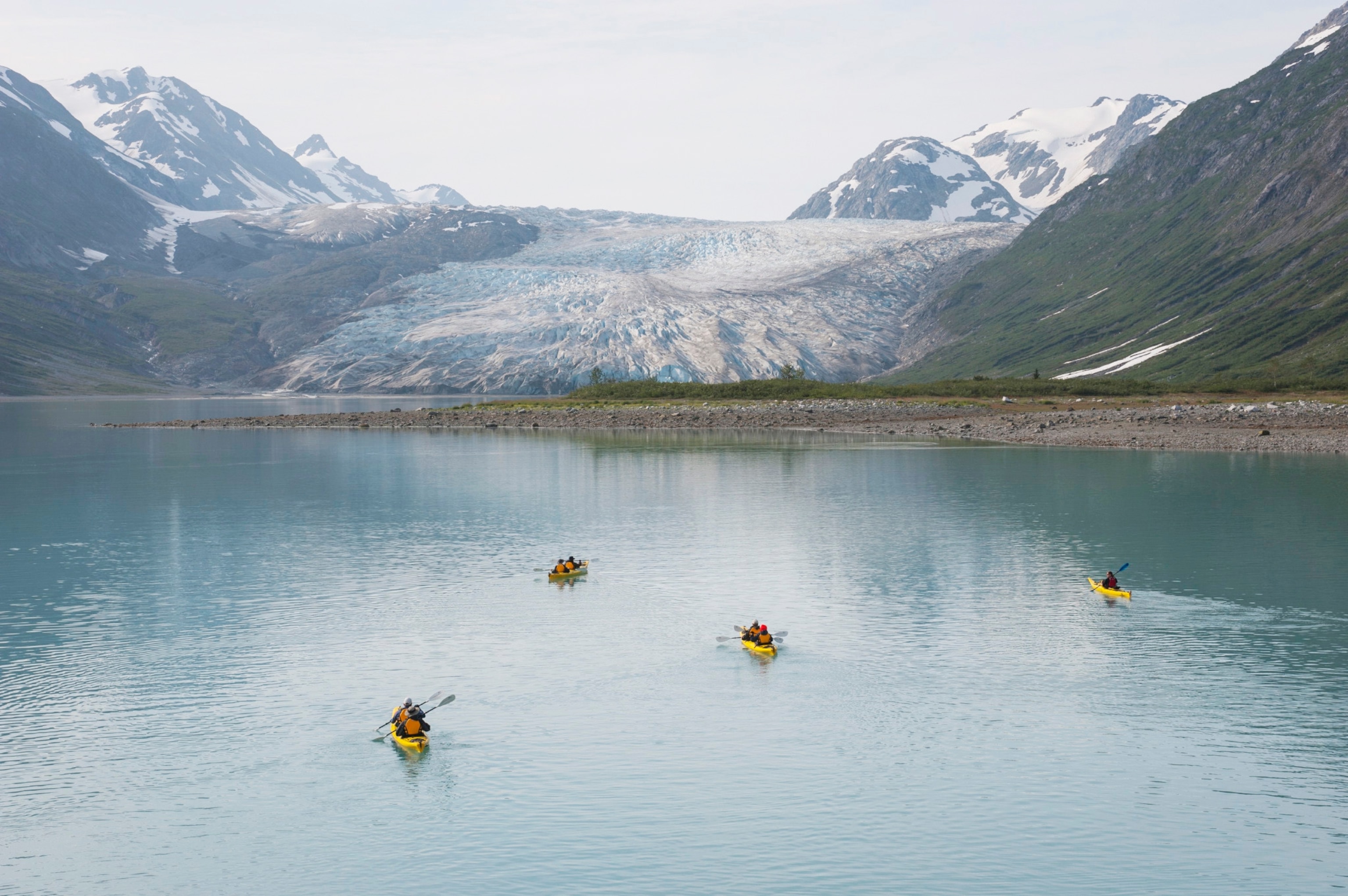 People kayaking in milky blue waters by a glacier