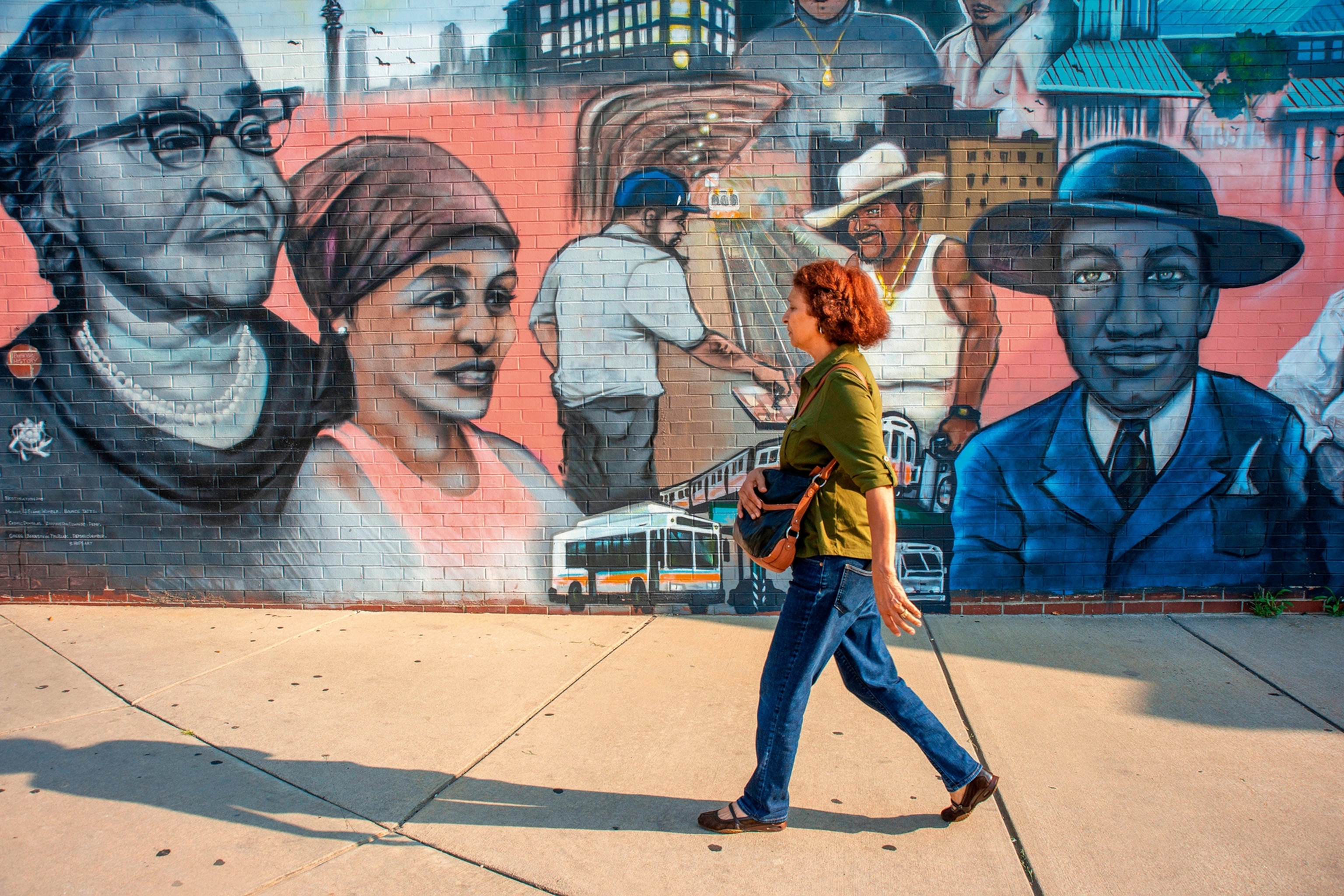 A woman walking past a mural depicting scenes of Black history.