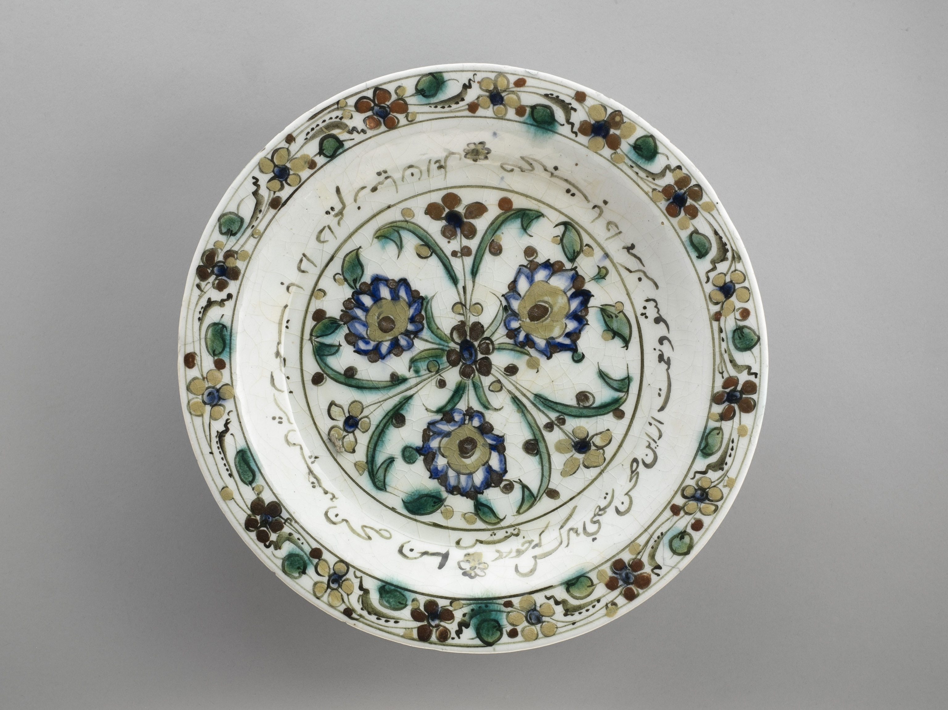A ceramic dish with painted plant decorations and Persian inscription.
