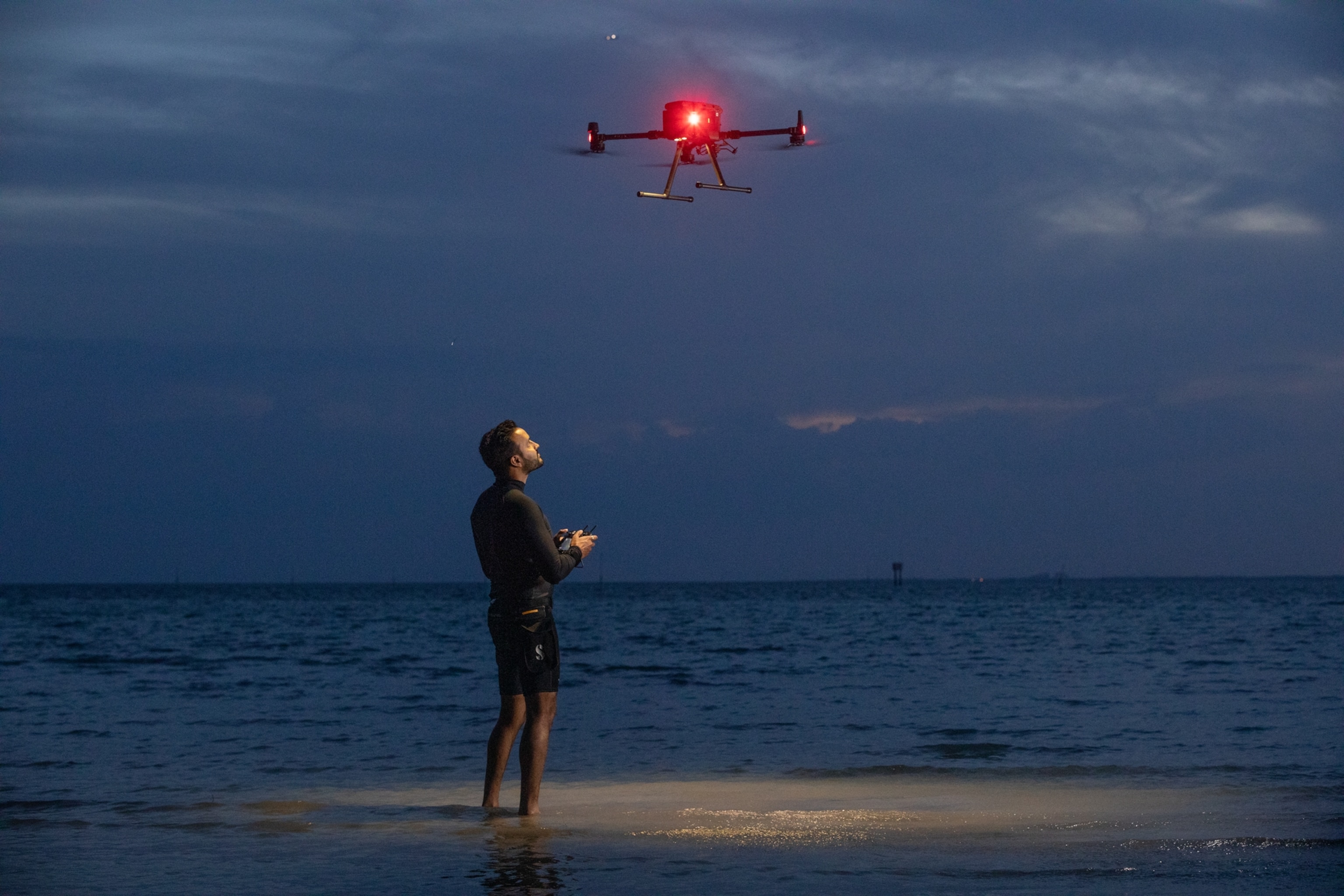 Picture of man operating drone over sea at night.