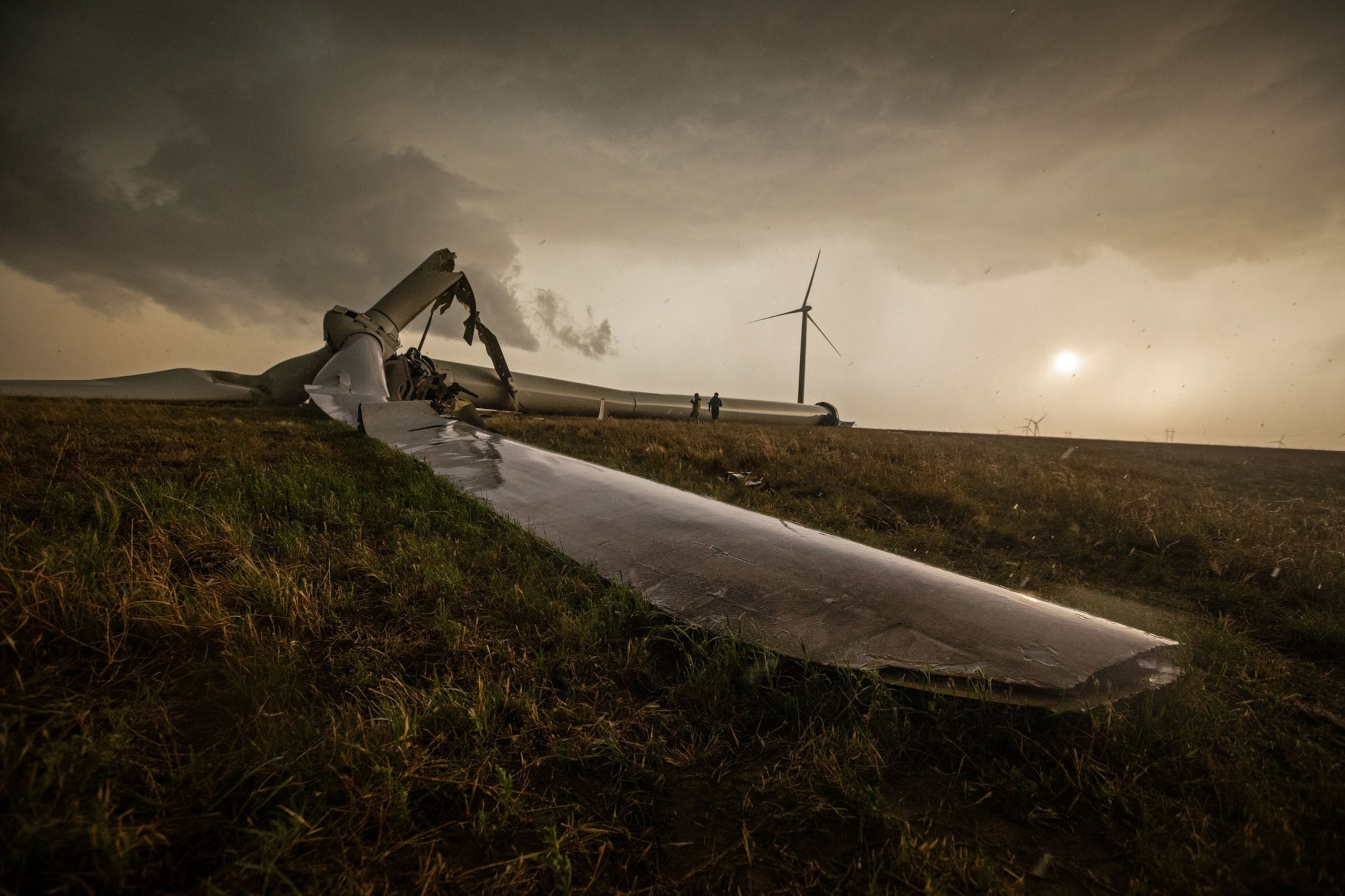 windmill blade on a ground with another windmill standing tall on background.