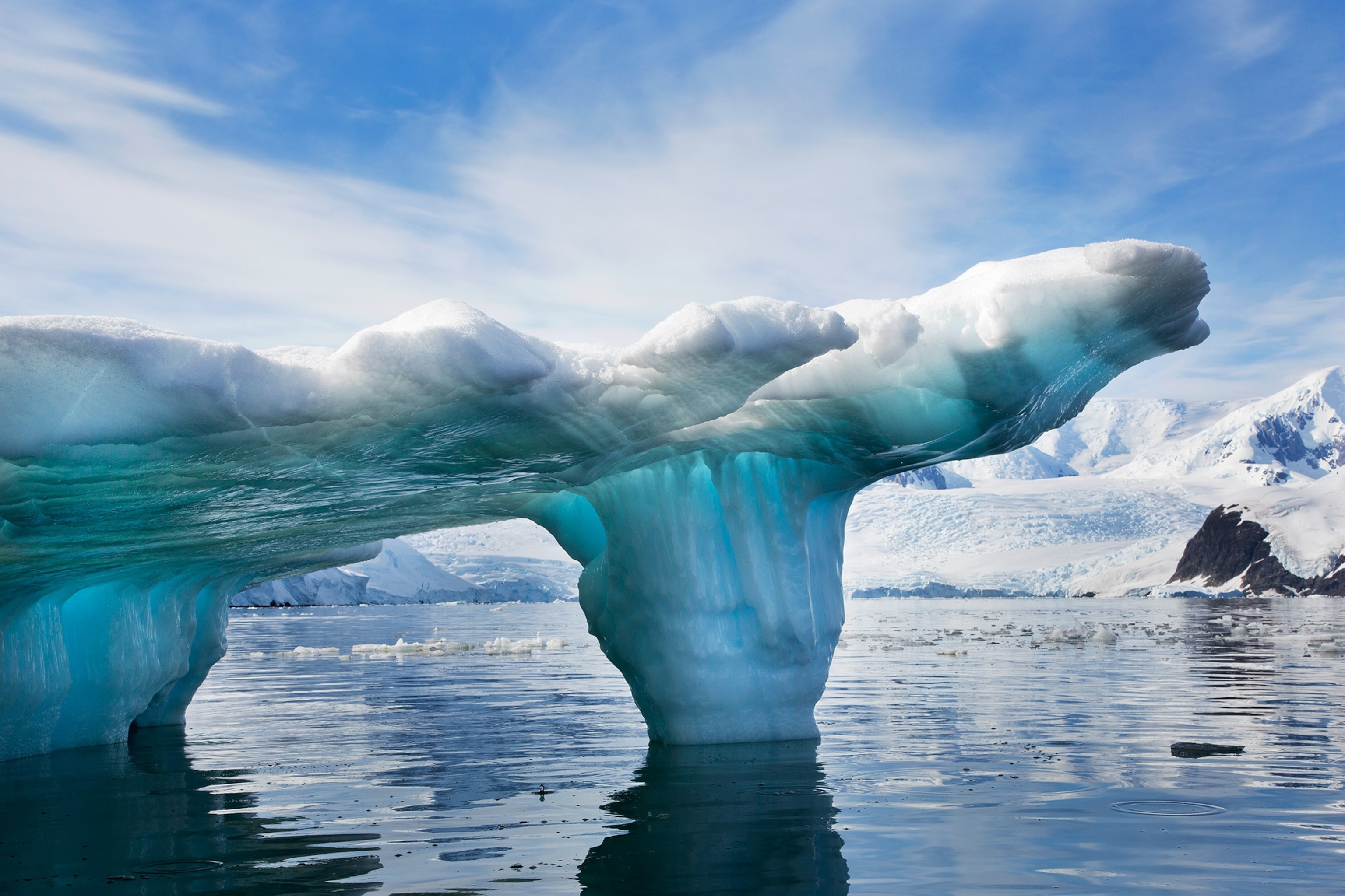 An Iceberg has various shades of blue and an archway on water.