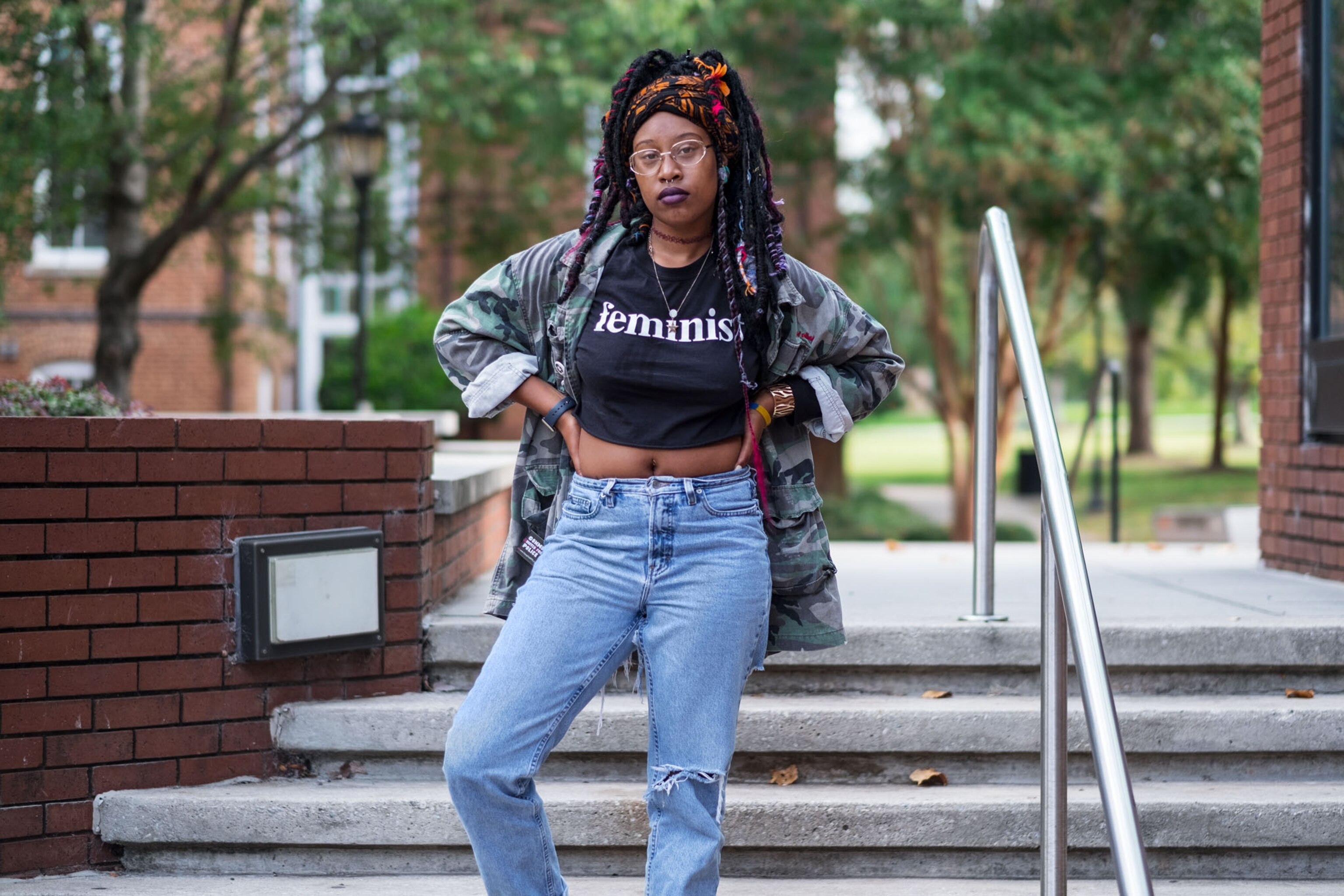 a young black woman wearing a back shirt that says "feminist" and blue jeans
