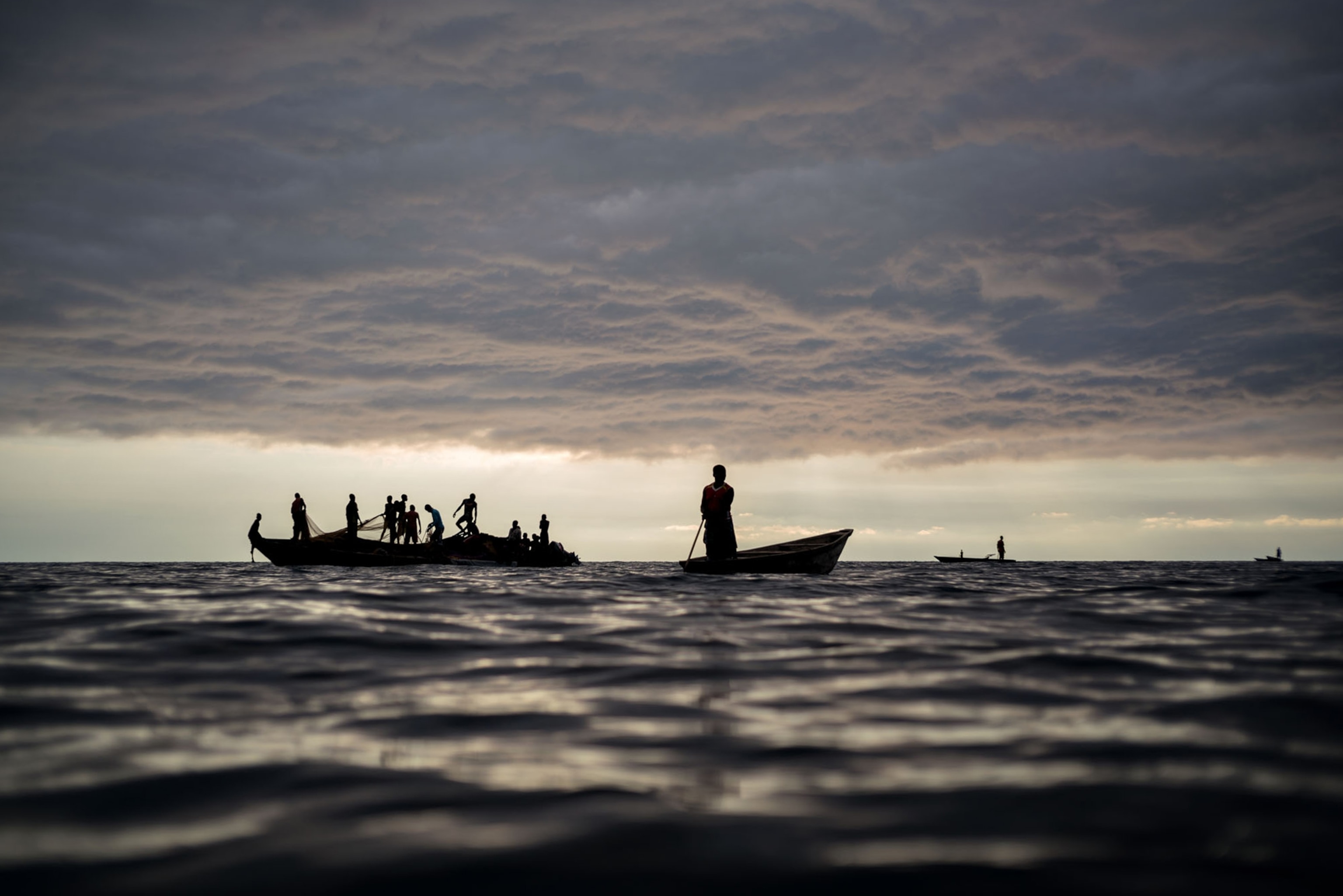 silhouetted boats with men casting nets to catch fish off shore