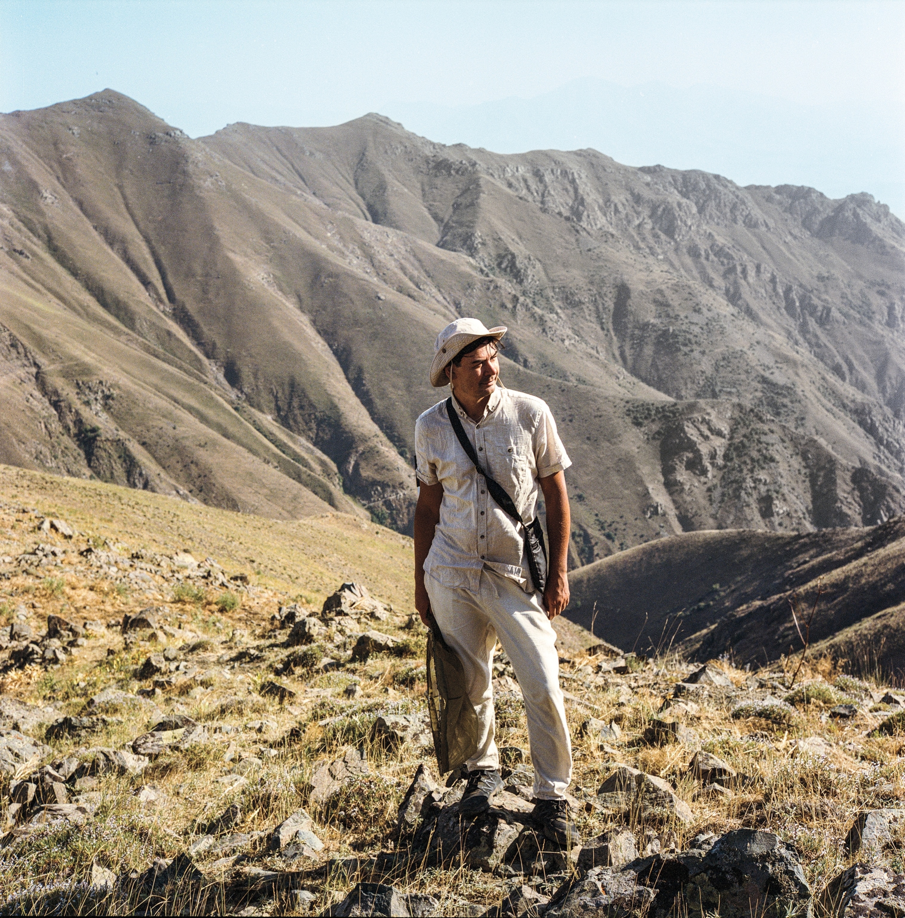 A man stands for a portrait with a view of mountains behind him.